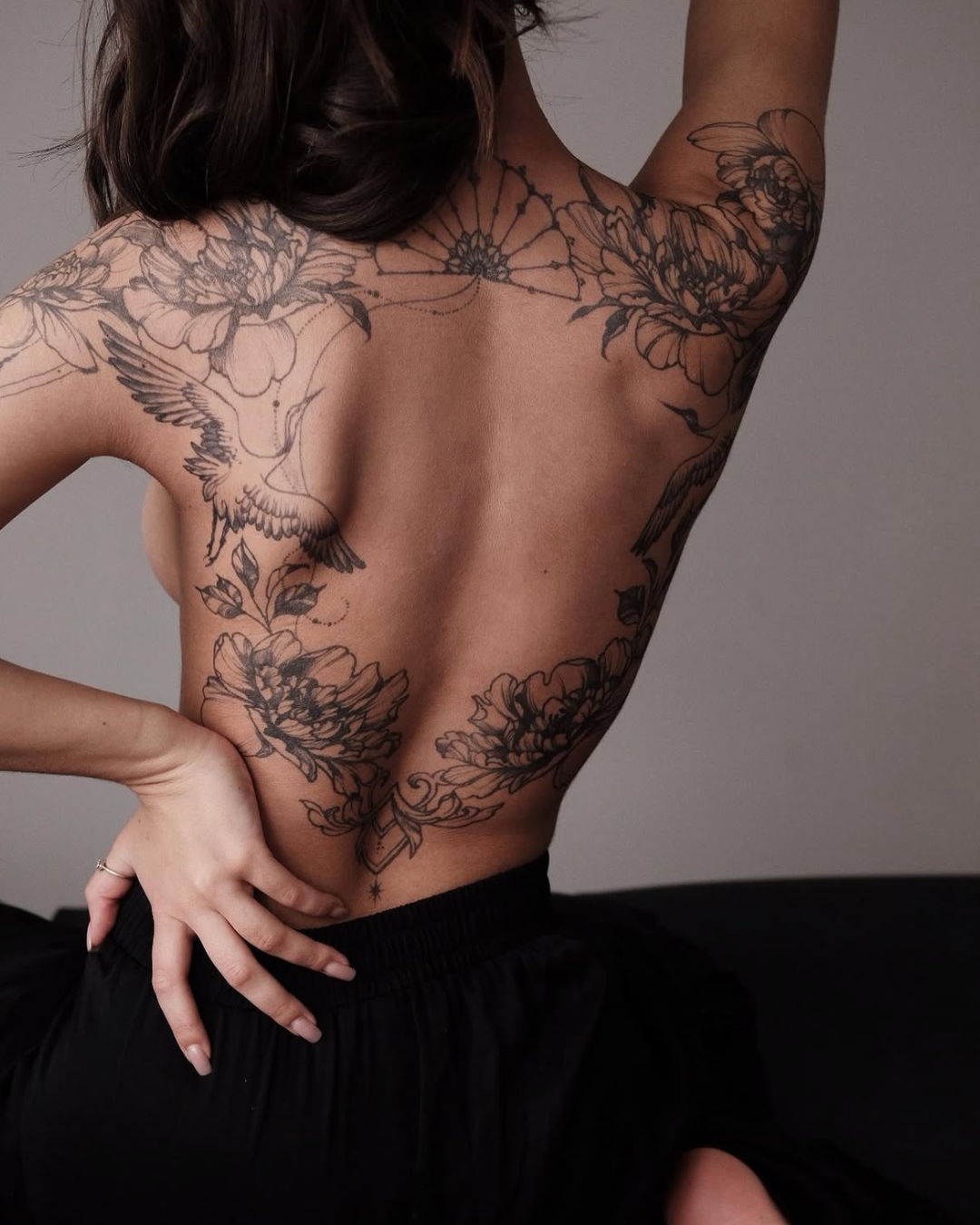 Fine line back tattoo framing the spine with peonies, flying cranes and an ornamental fan with dotwork chains by @VERONICALILU