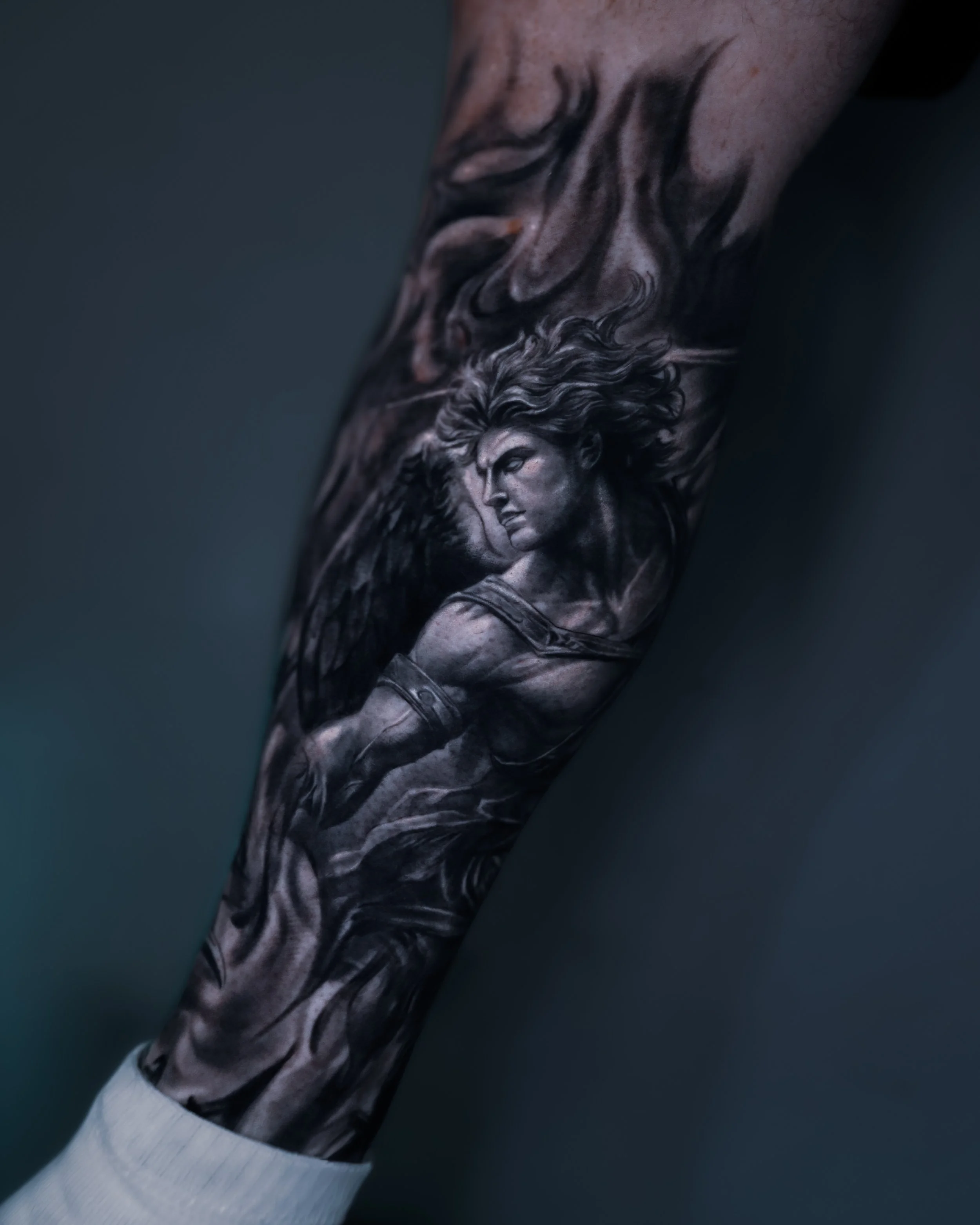 Black and grey fallen angel tattoo with wings and flowing hair on forearm by Andrei Cotici at FYNE Leeds