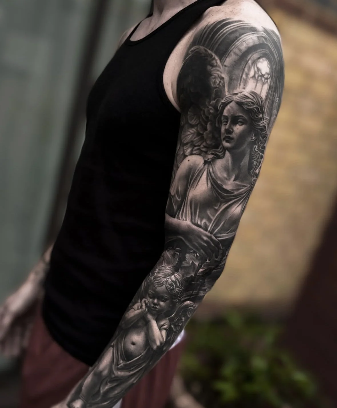 Black and grey weeping angel statue full sleeve tattoo with cherub detail by Andrei Cotici at FYNE Leeds