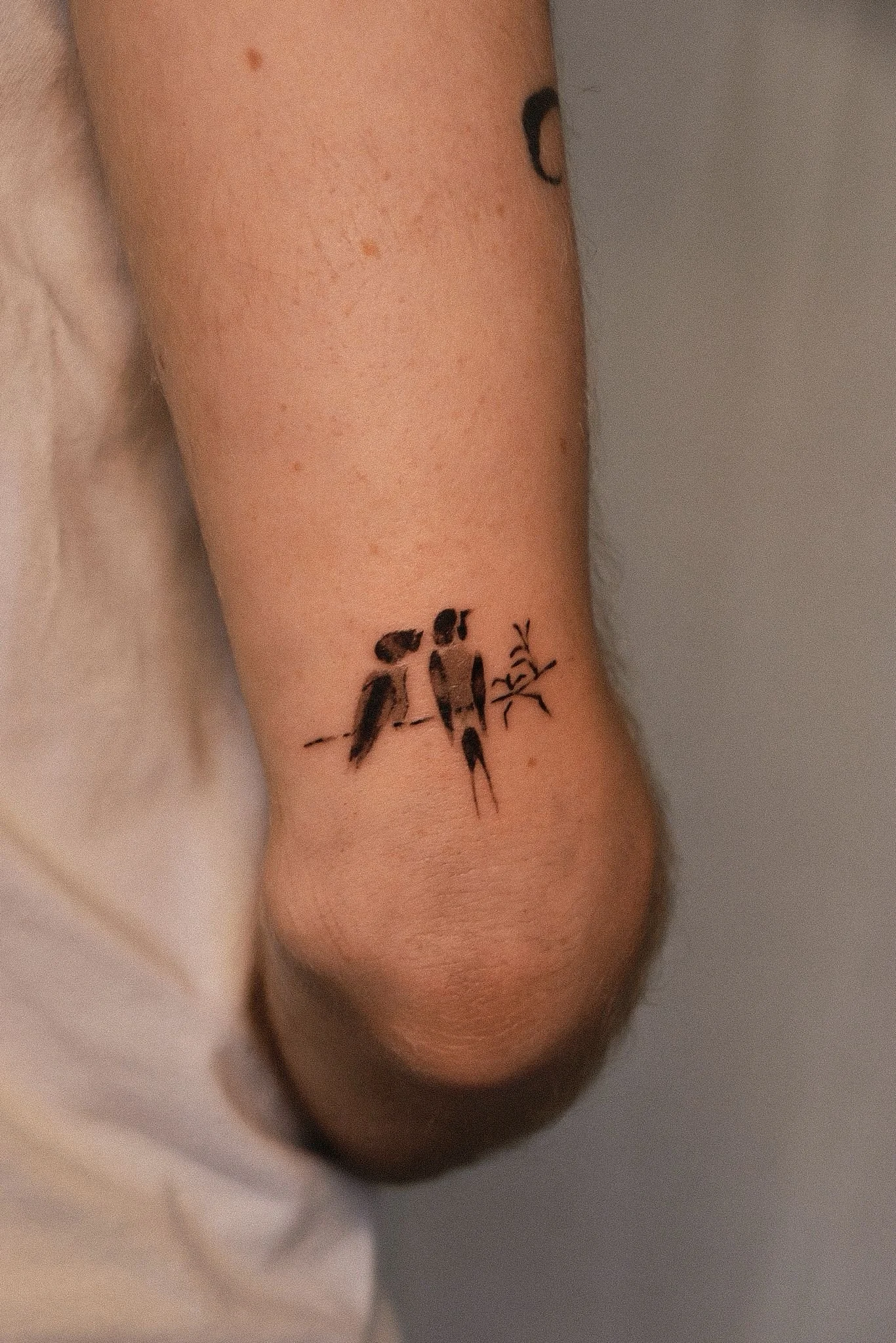 Close-up of a person's wrist with a small black tattoo of a branch with leaves.