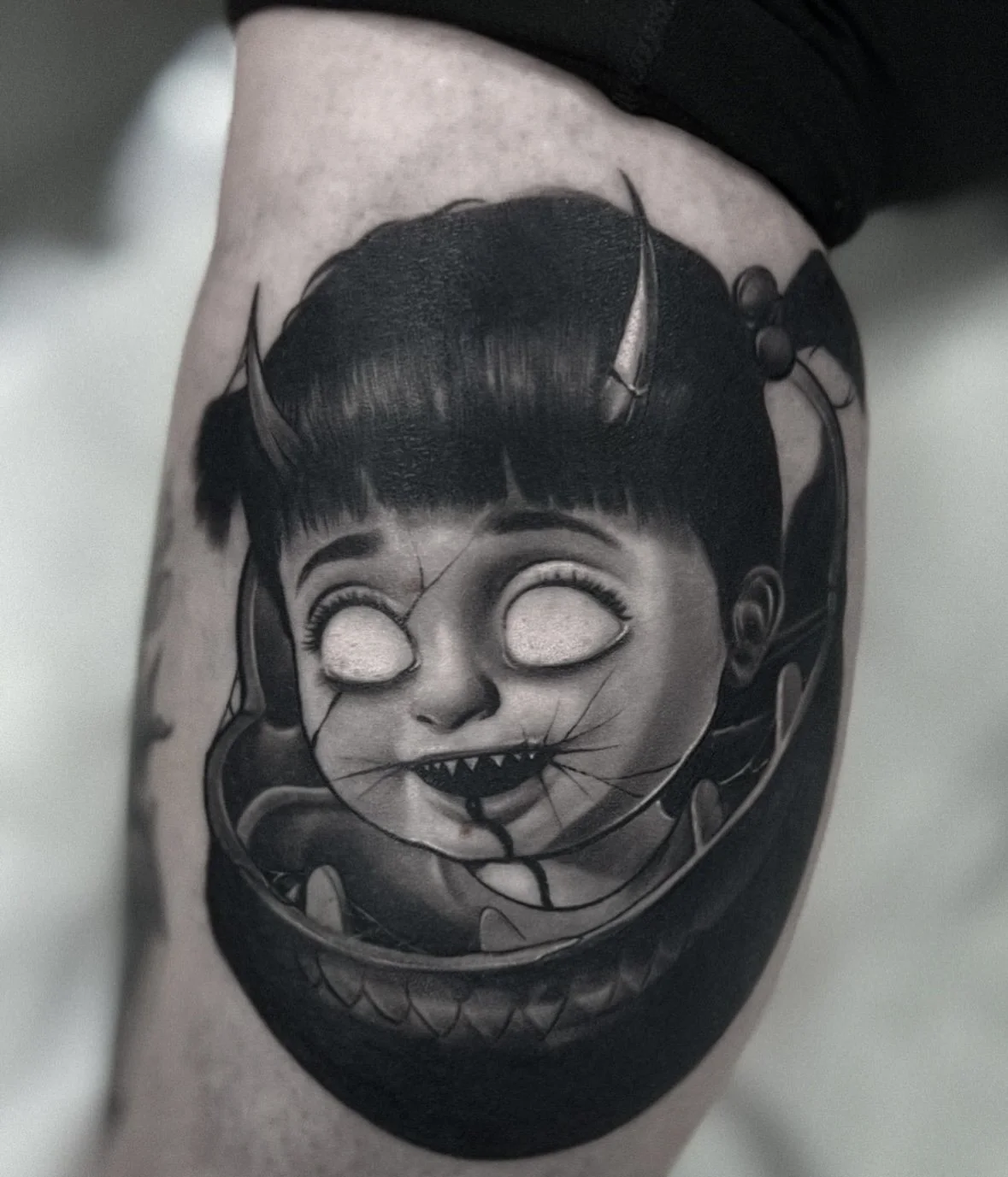 Black and grey horror doll tattoo with cracked face and horns on upper arm by Andrei Cotici at FYNE Leeds