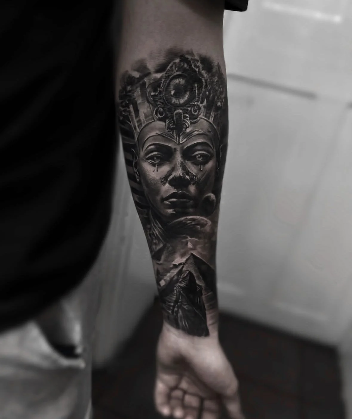Black and grey realism Egyptian pharaoh portrait tattoo with all-seeing eye headdress and pyramids on forearm by Andrei Cotici at FYNE Leeds