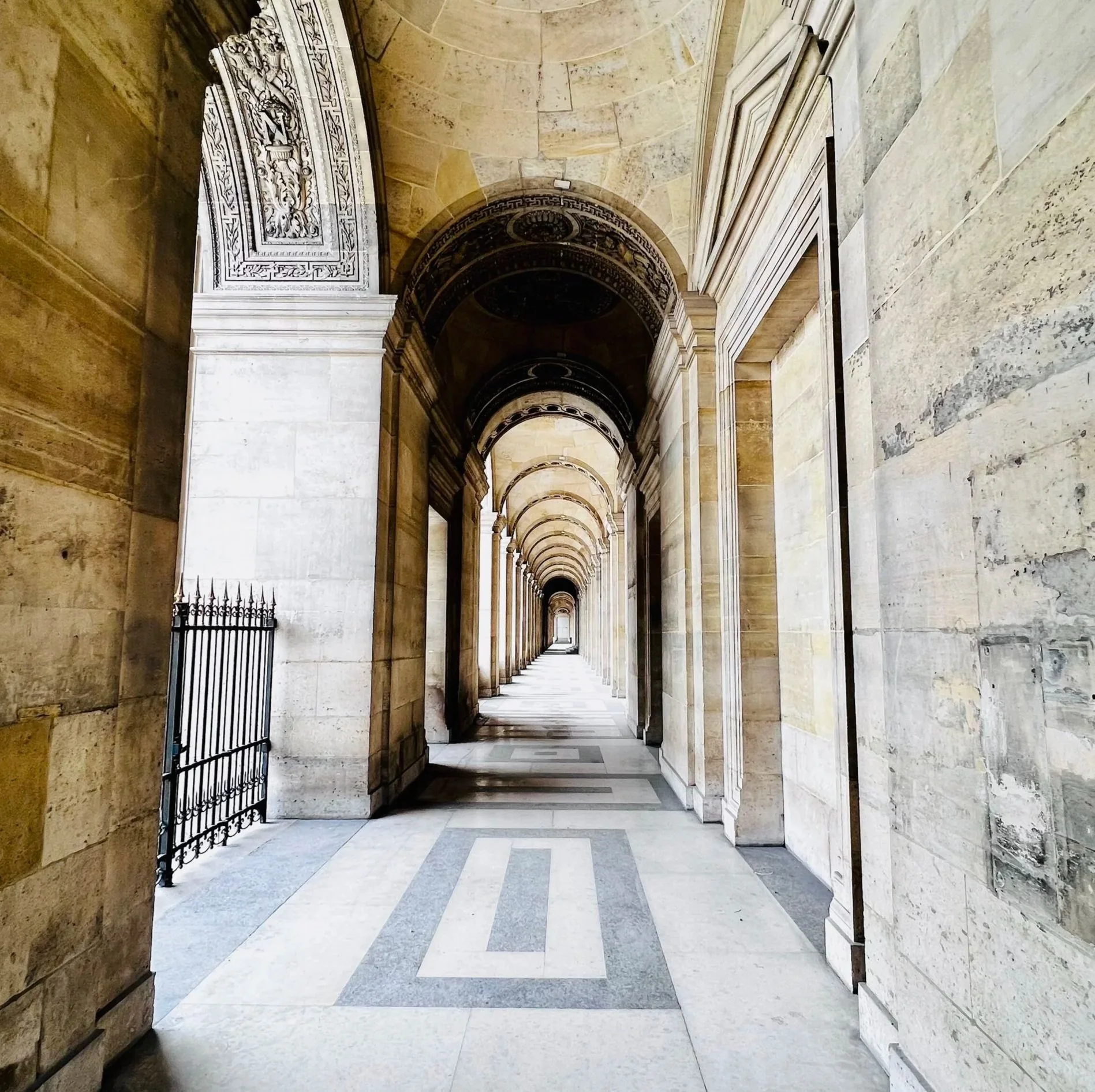 Long stone corridor with arches and columns, featuring detailed architectural work, leading to a distant door or opening.