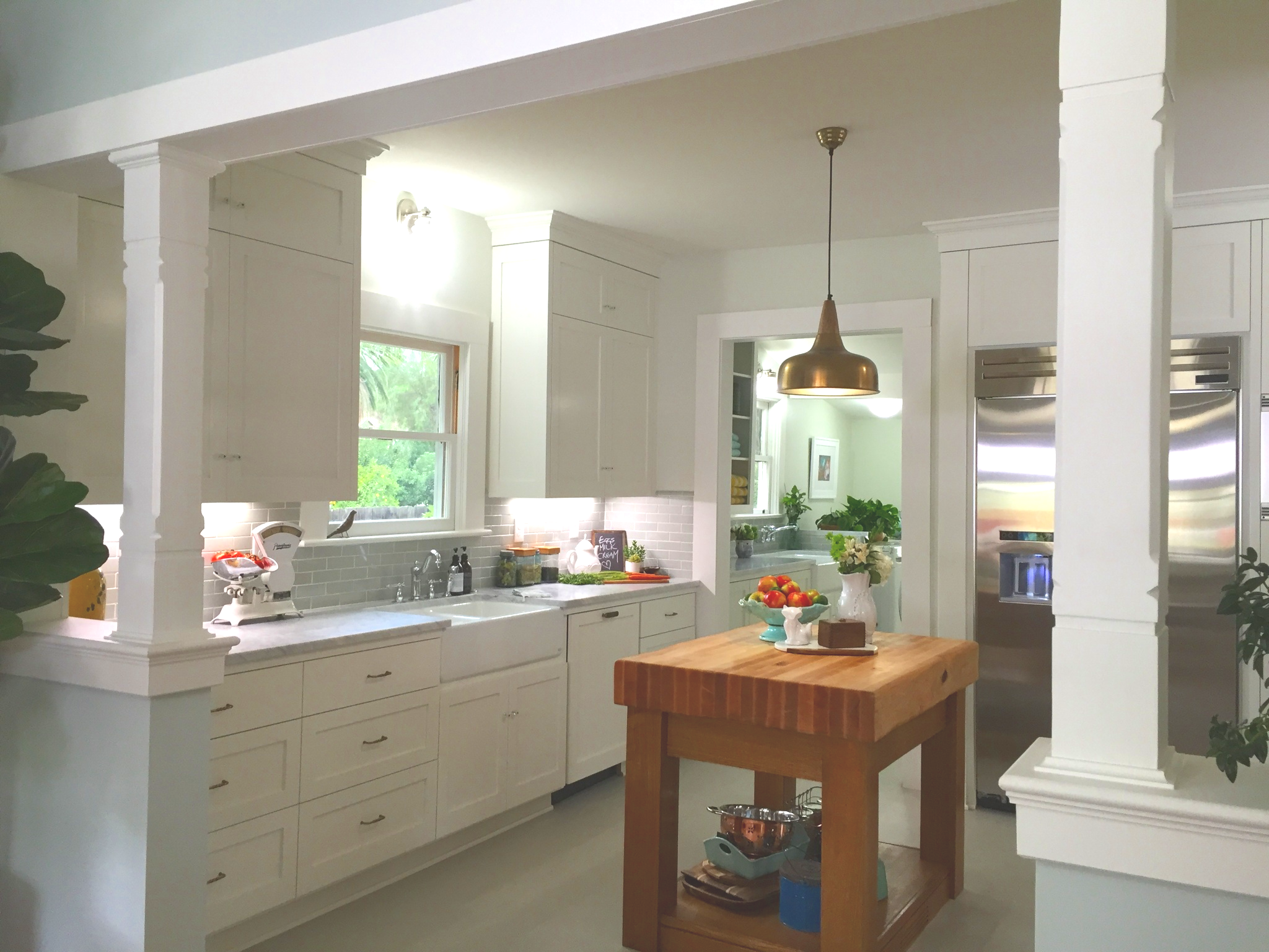 Bright kitchen with white cabinets, a window over the sink, a wooden island with fruit on top, and a stainless steel refrigerator.