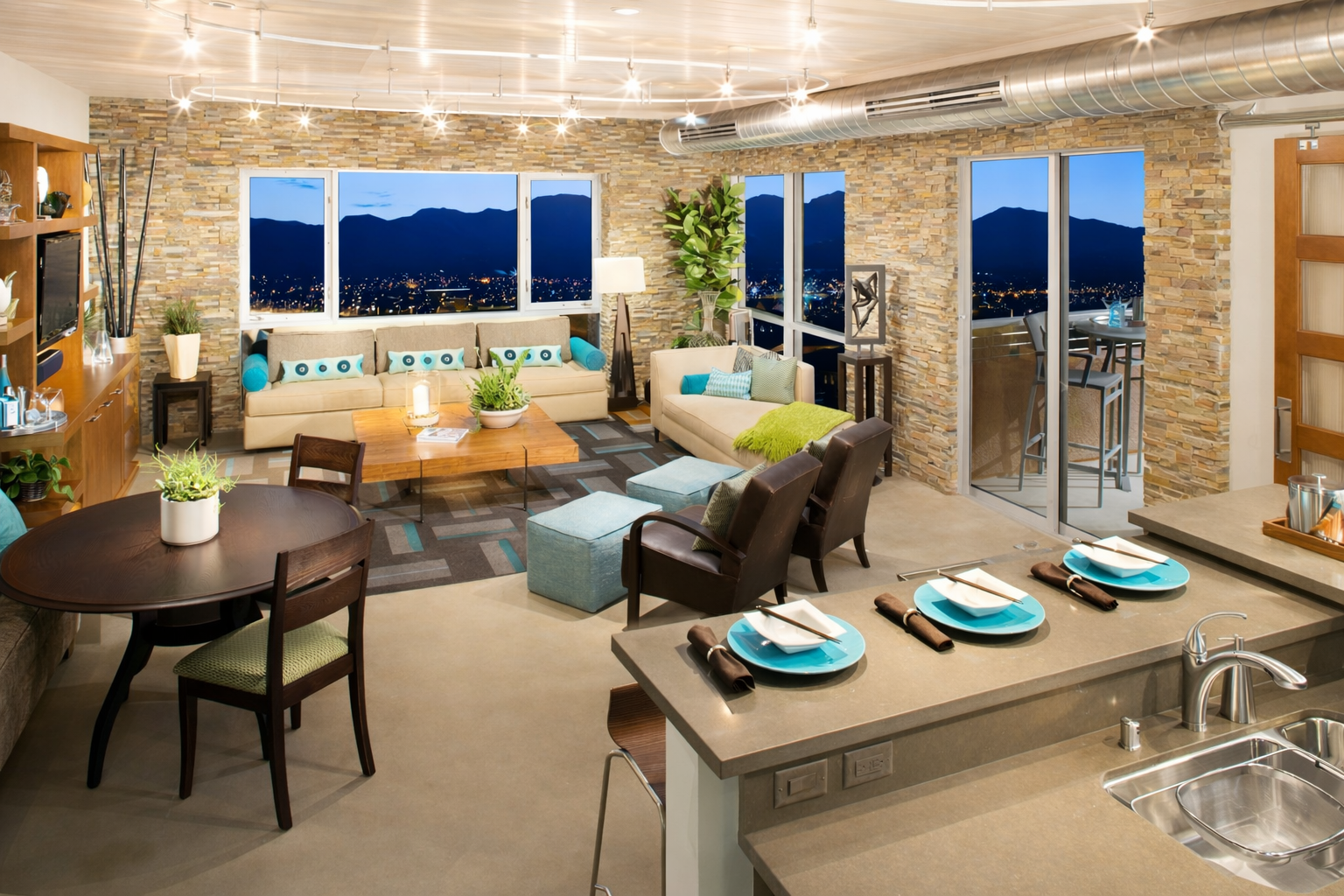 Open-concept living room and dining area with large windows showing a mountain view at night, decorated with modern furniture and plants.