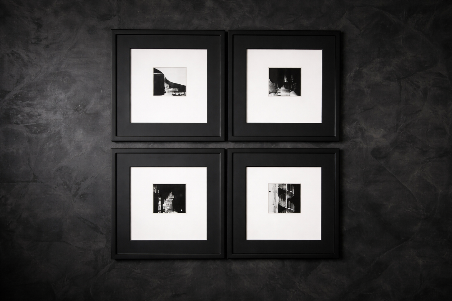 Four black and white photographs framed in black, arranged in a 2x2 grid on a dark textured wall.
