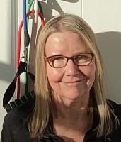 Woman with glasses and long hair smiling indoors.