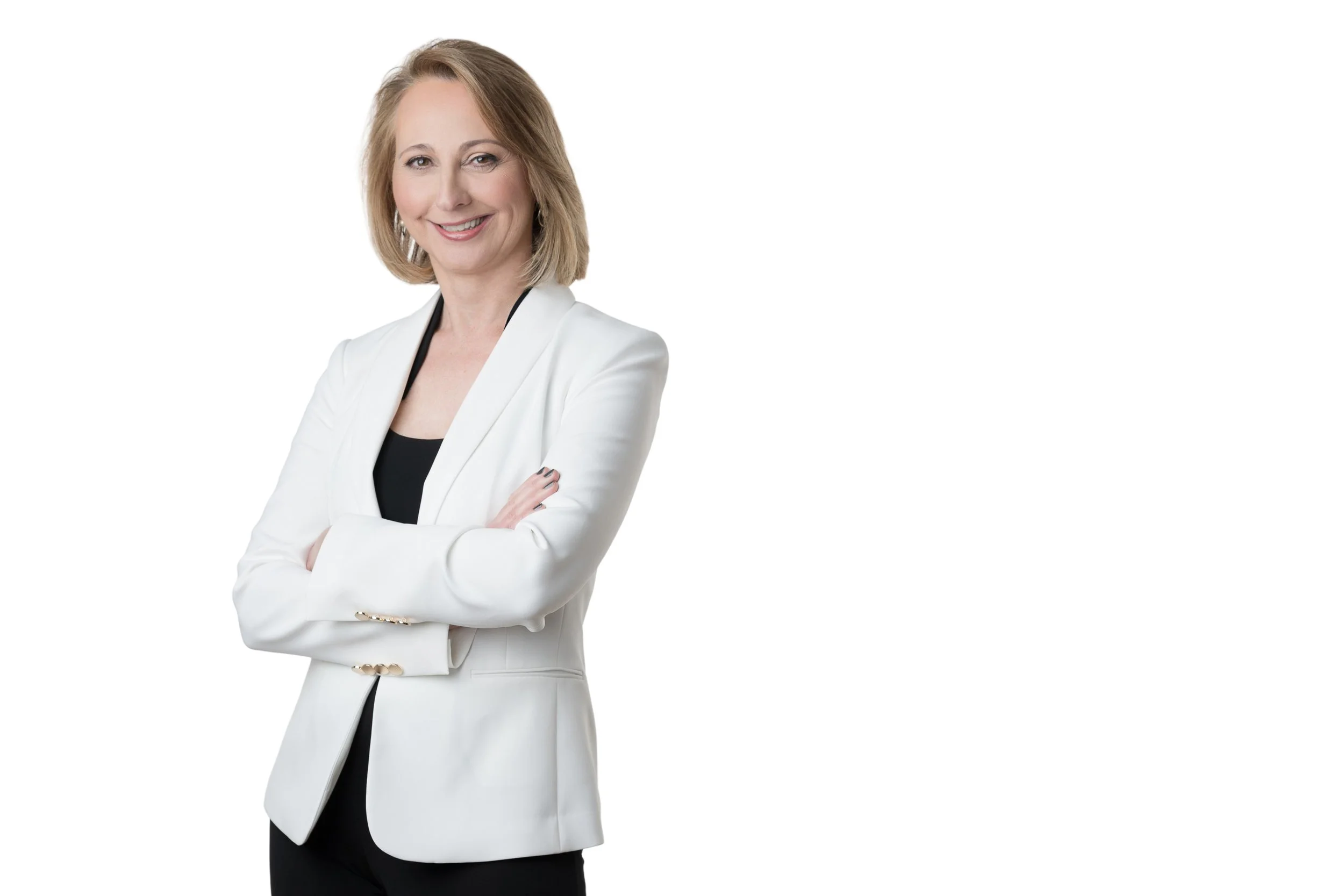 A woman with blonde hair wearing a white blazer and black top, smiling with arms crossed against a white background.