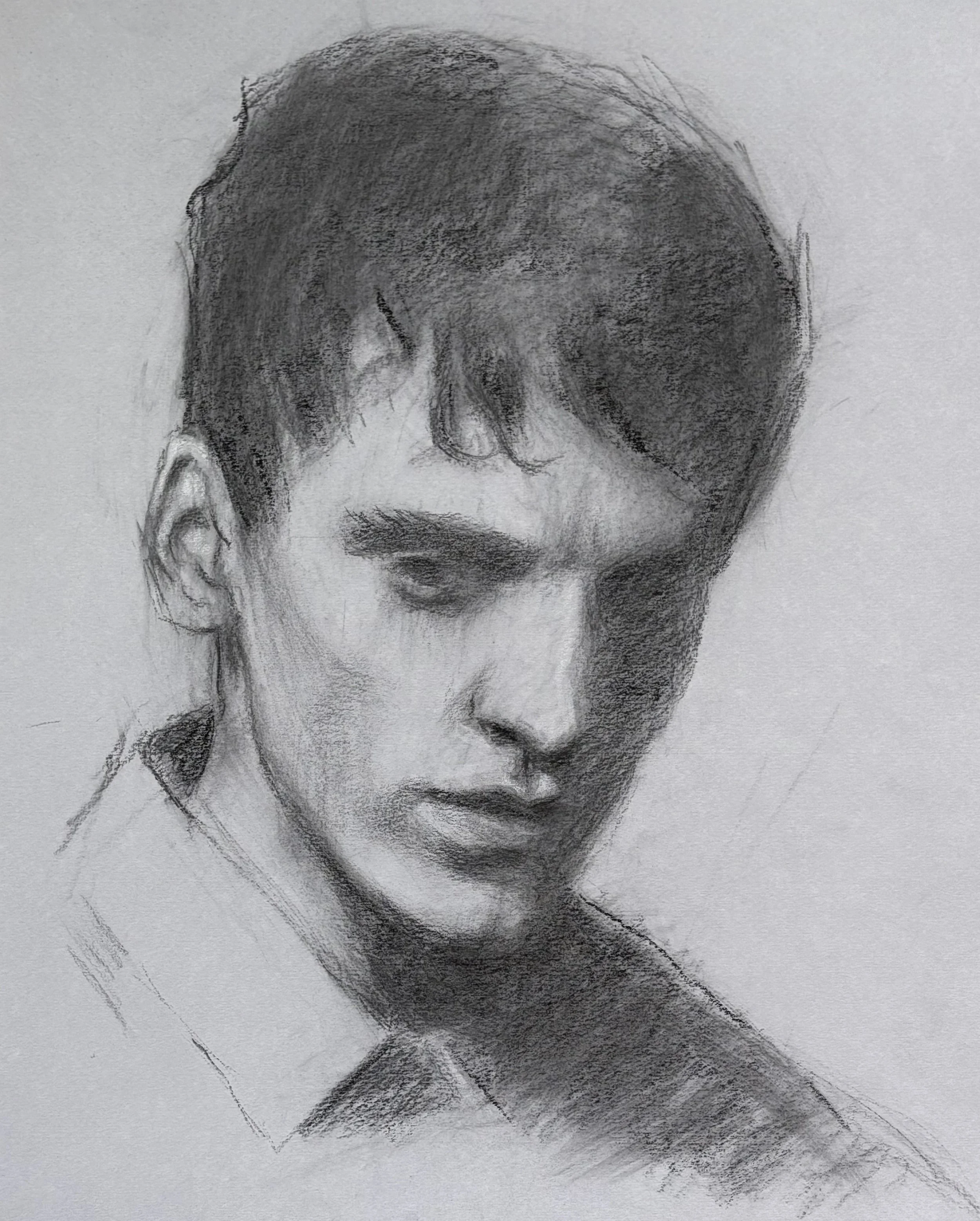 A graphite sketch of a young man with short hair, slightly parted lips, wearing a collared shirt, looking down with a contemplative expression.