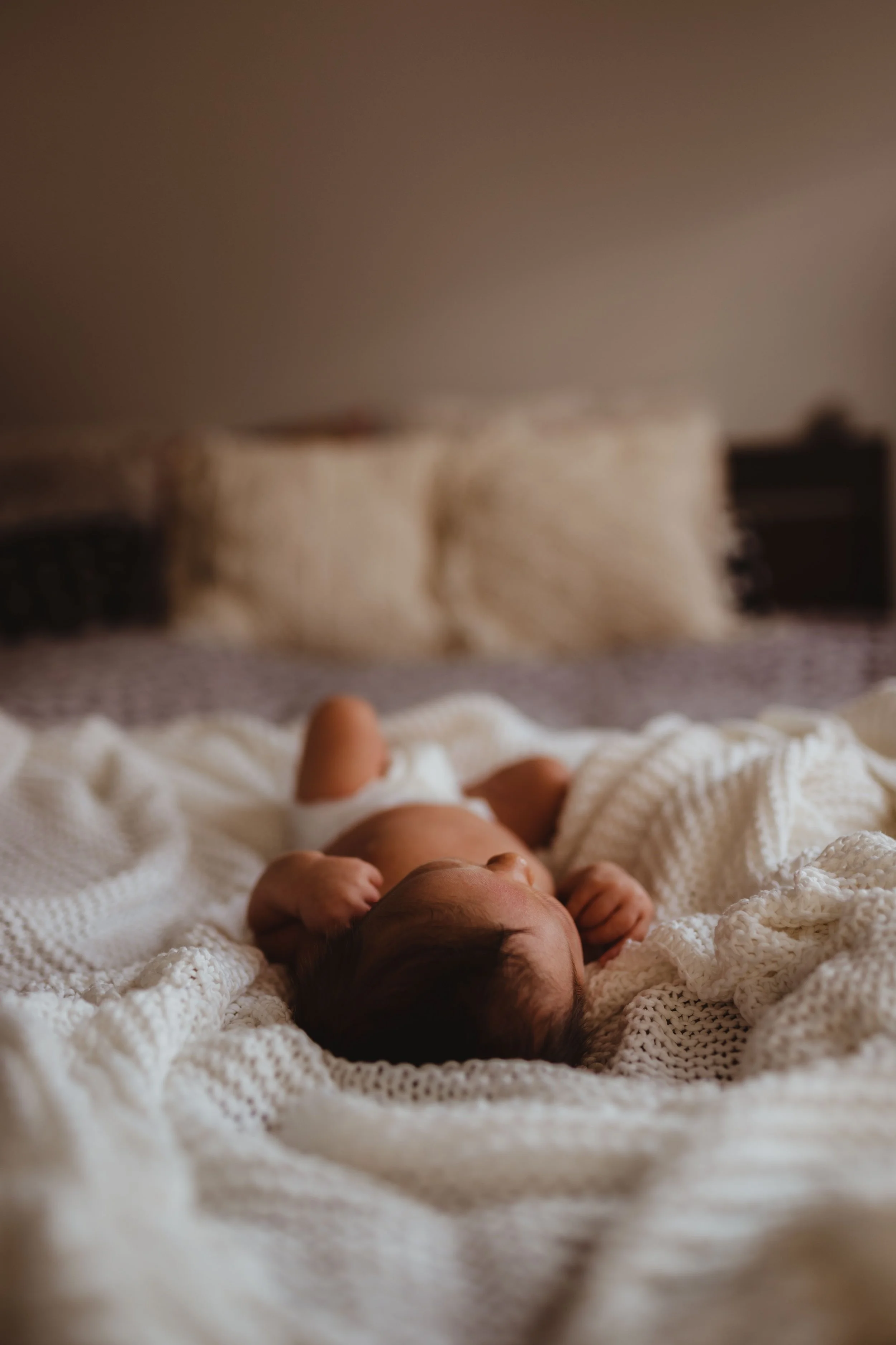 Bébé allongé sur un lit enroulé dans une couverture blanche, vue de face, avec des meubles sombres en arrière-plan.