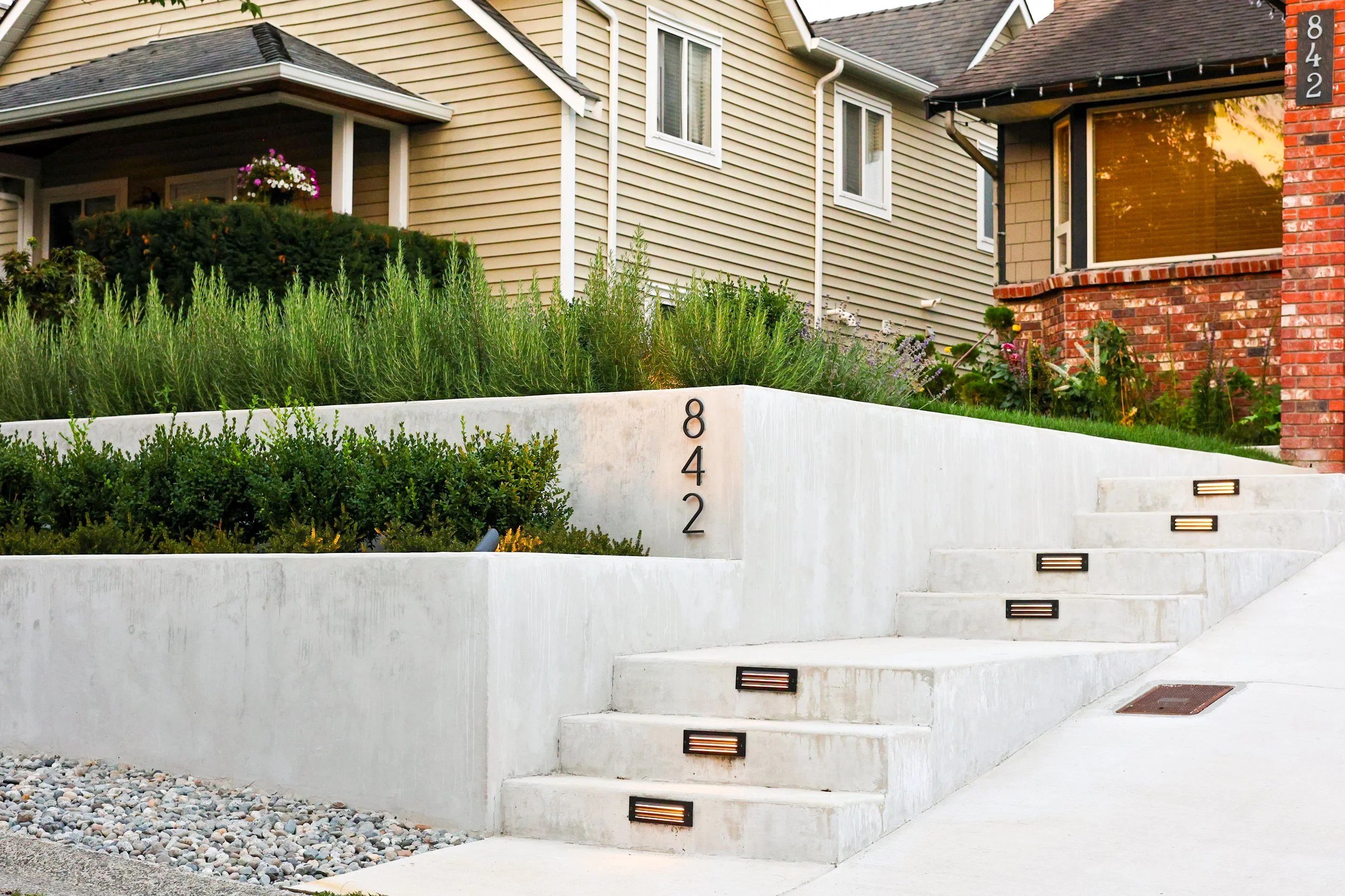 Residential house with beige and red brick exterior, concrete stairs with built-in lighting, and house number 842 displayed on a white wall.