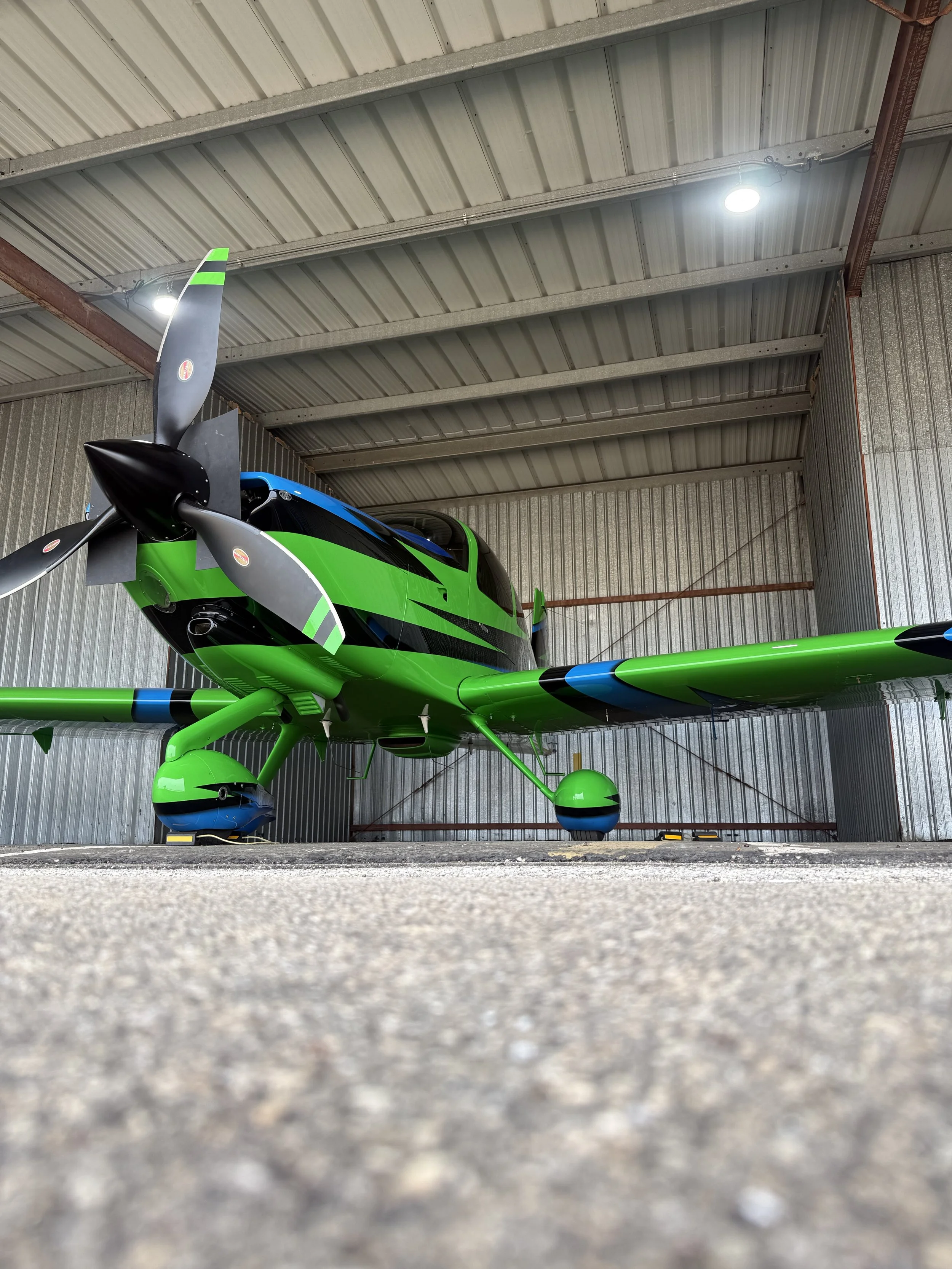 A green and black helicopter parked inside a metal storage shed with a corrugated metal roof.
