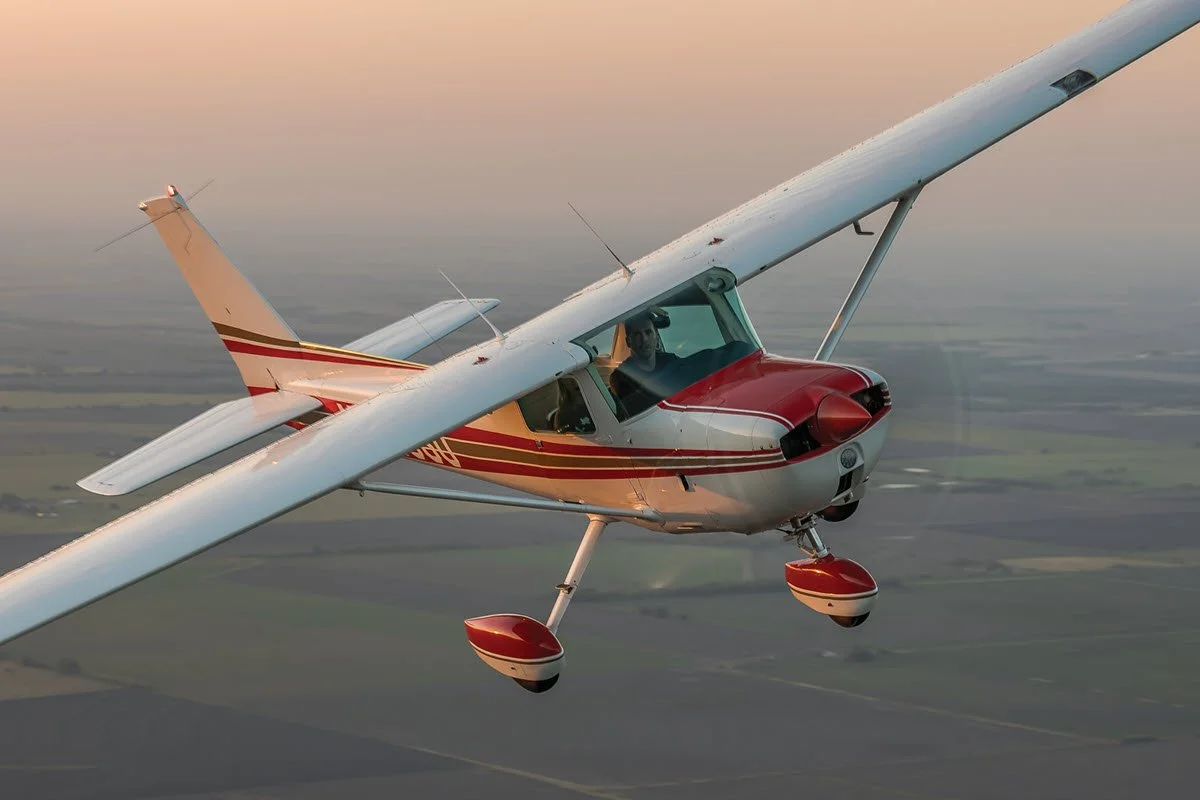 Small single-engine airplane flying over farmland at sunset.