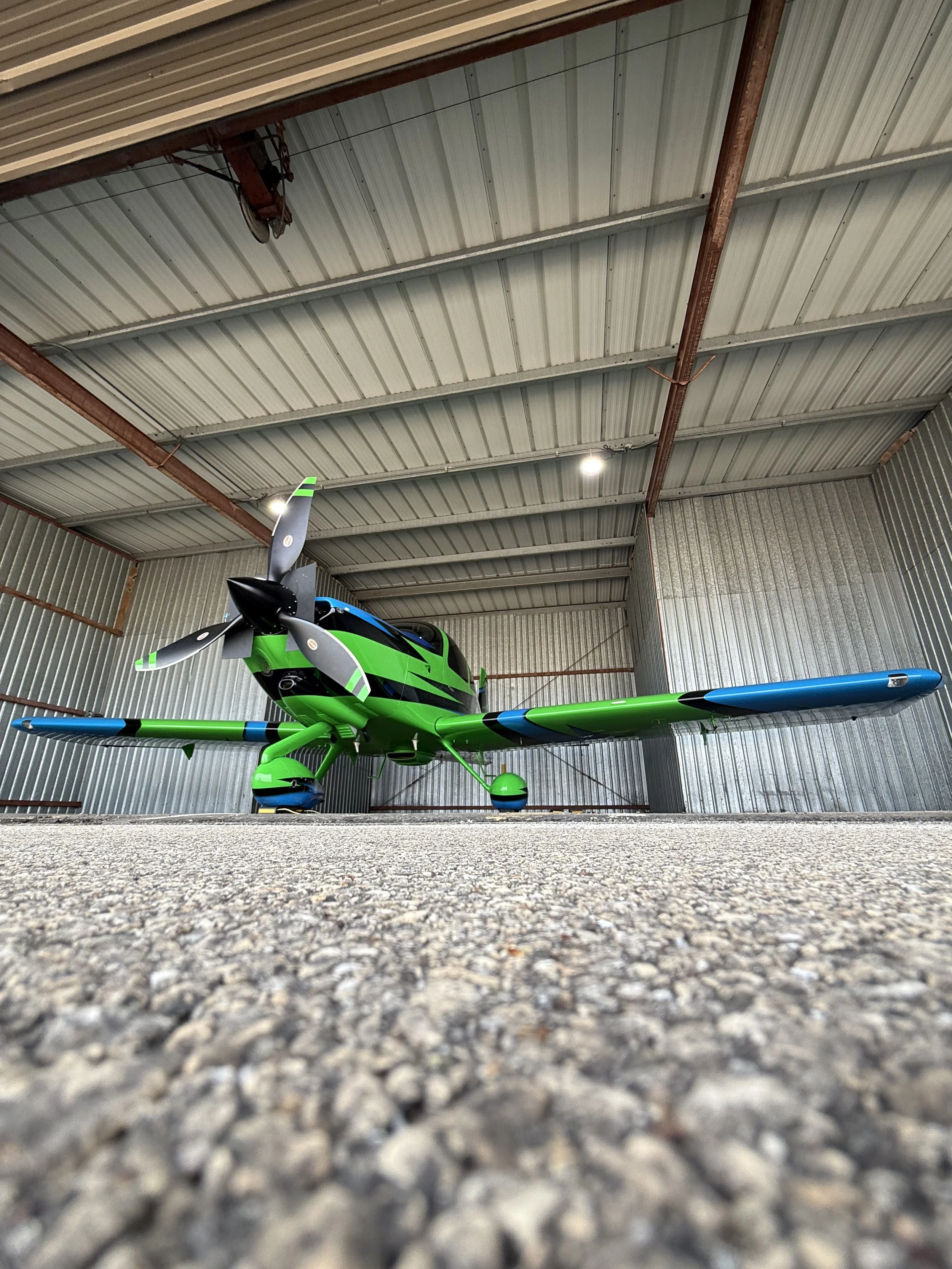 A green and black remote-controlled airplane stored inside a metal hangar with a concrete floor.