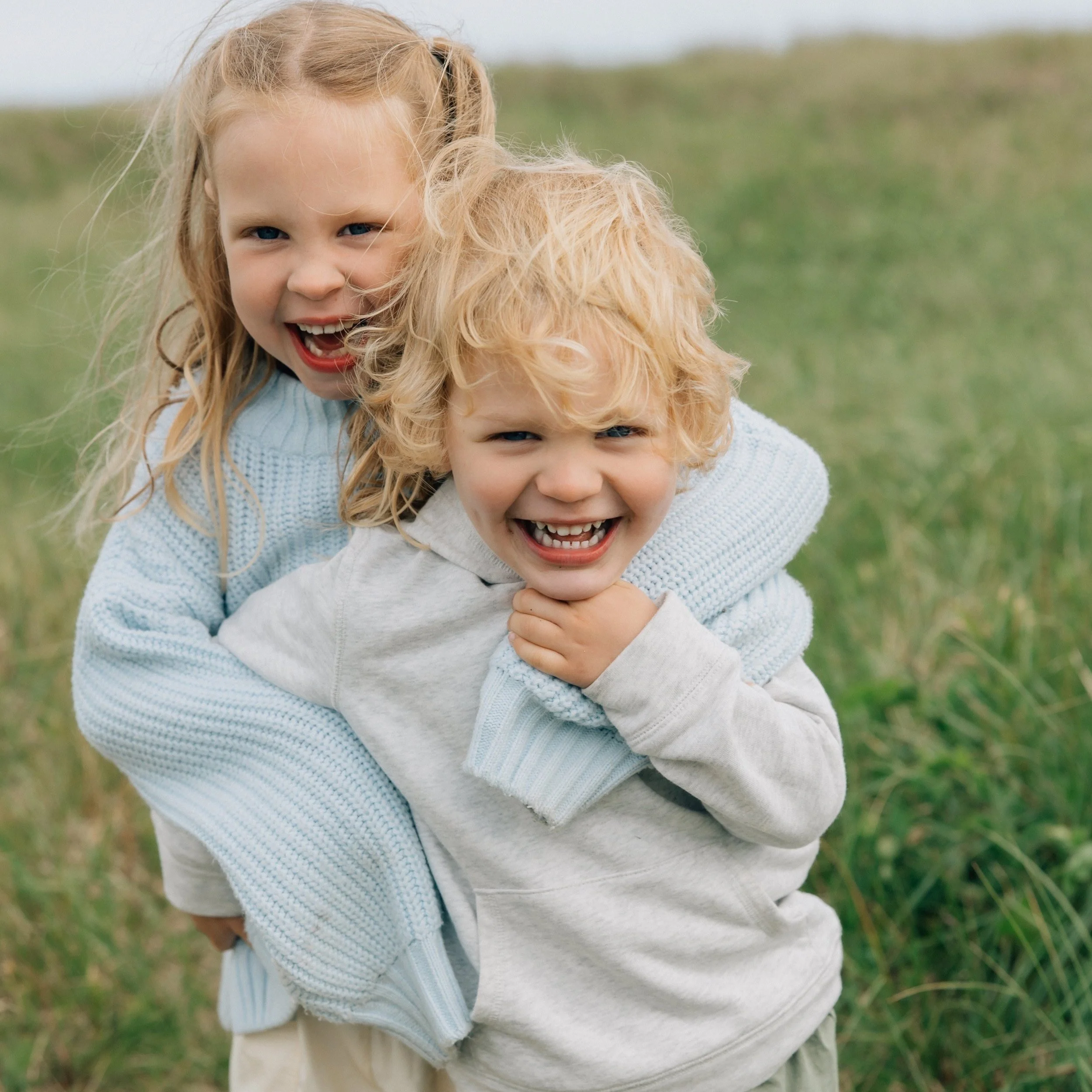 Two children, a girl and a boy, laughing and playing outdoors in a grassy field.