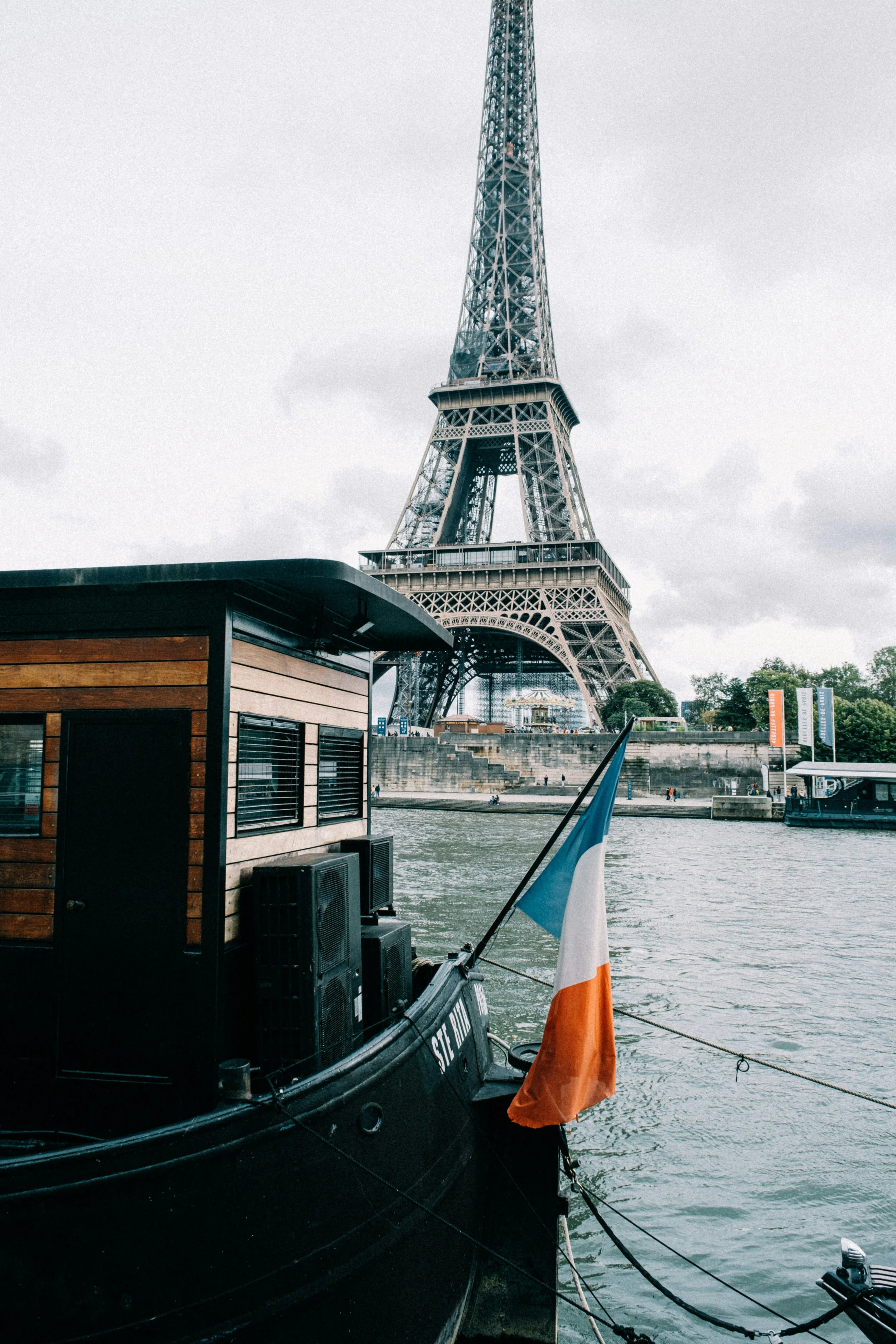 View of the Eiffel Tower from a boat on the Seine River in Paris, France, with the French flag visible on the boat.