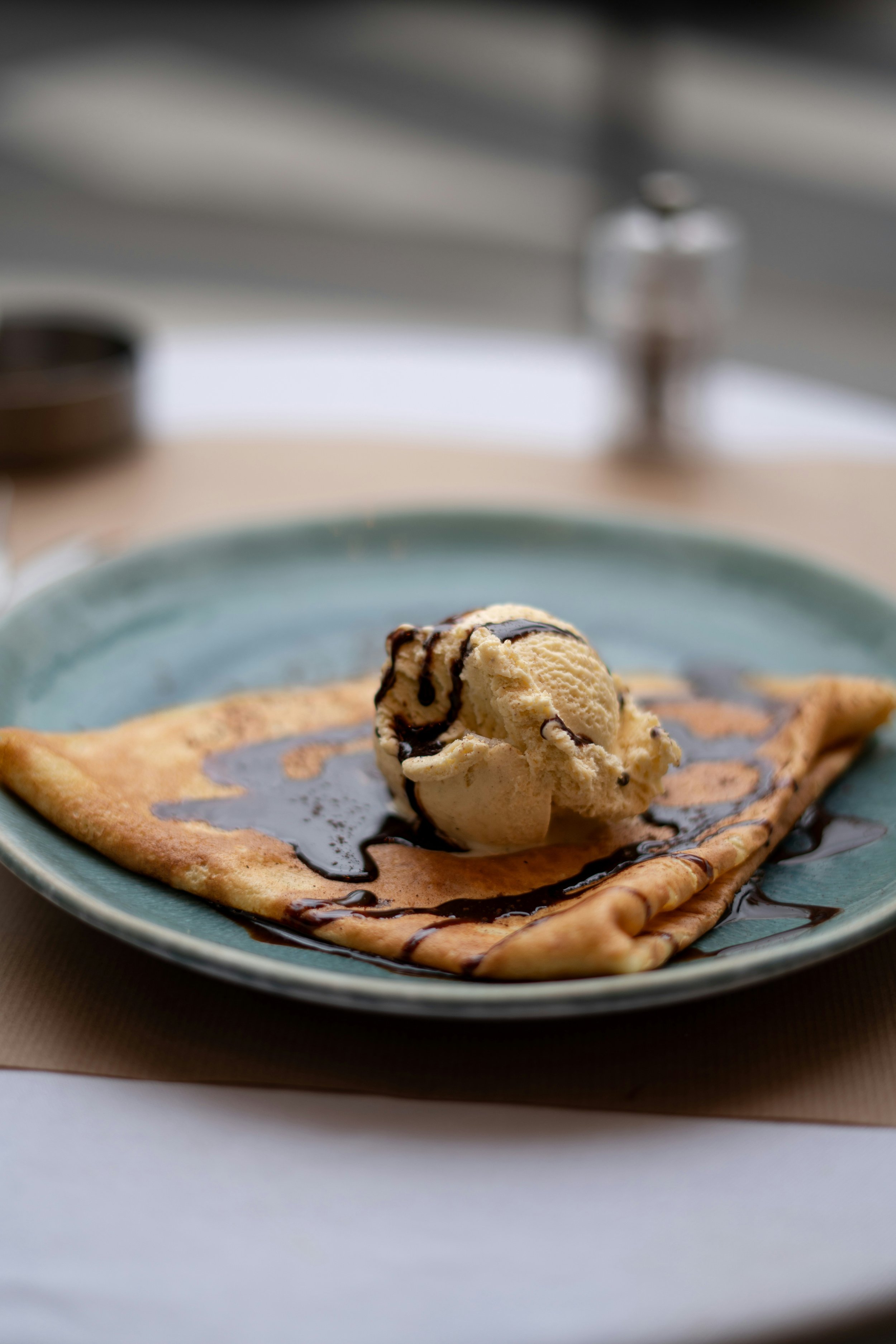 A crepe topped with a scoop of vanilla ice cream drizzled with chocolate sauce on a turquoise plate. VOYA curates bespoke travel experiences in France and Napa Valley.