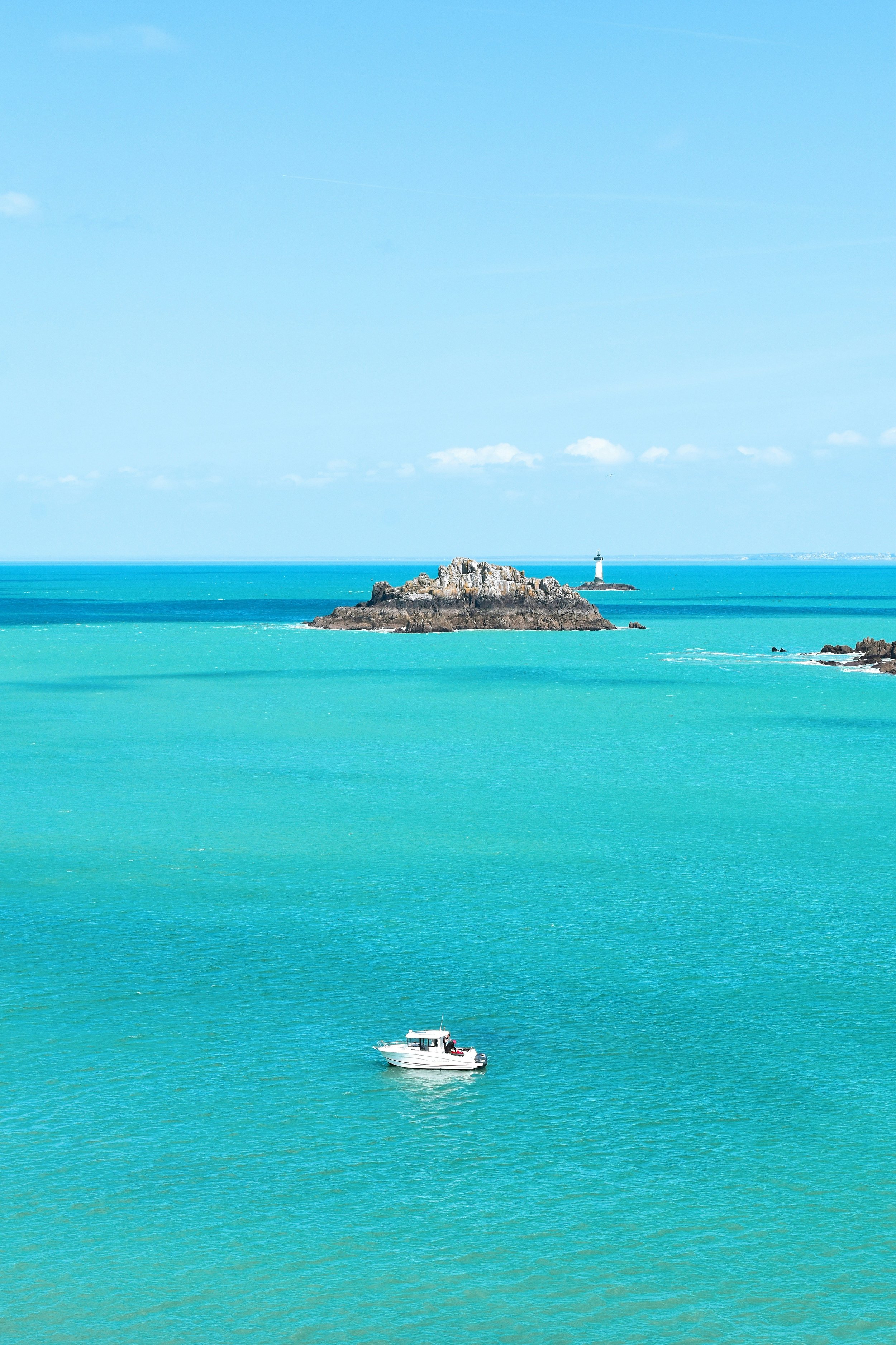A boat floating on turquoise water near a small rocky island with a lighthouse in the distance. VOYA curates bespoke travel experiences in France and Napa Valley.