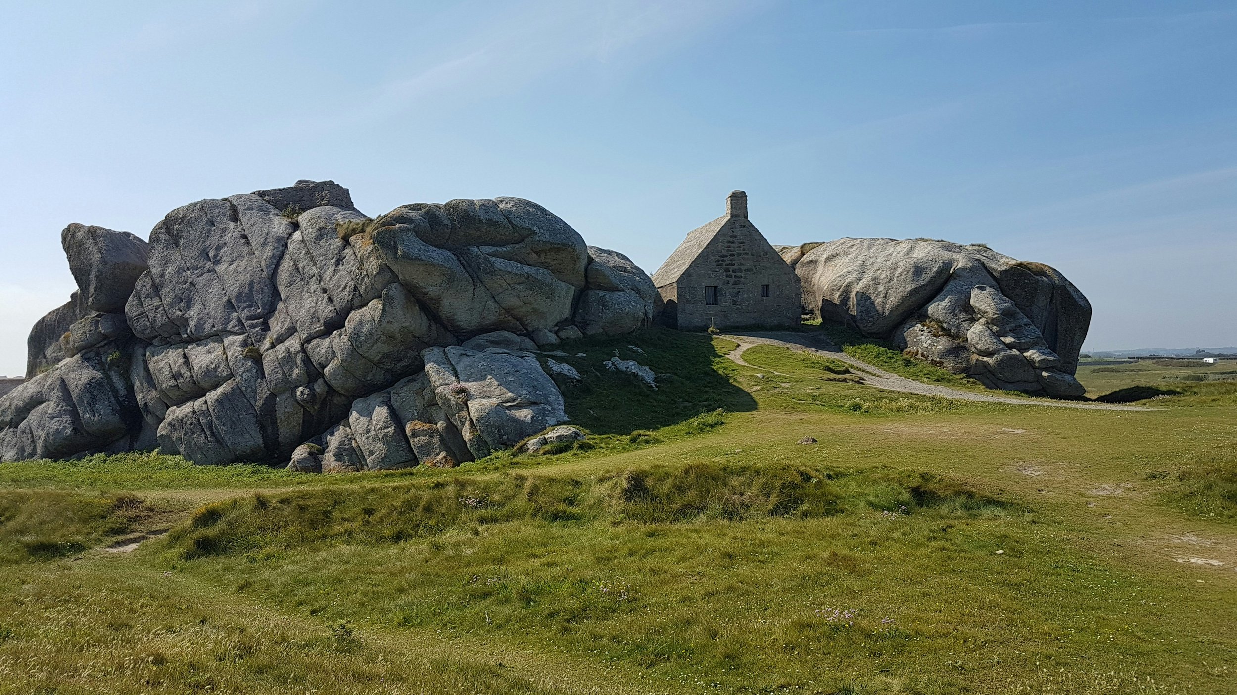 A small stone house situated among large rocks on a grassy landscape under a blue sky. VOYA curates bespoke travel experiences in France and Napa Valley.