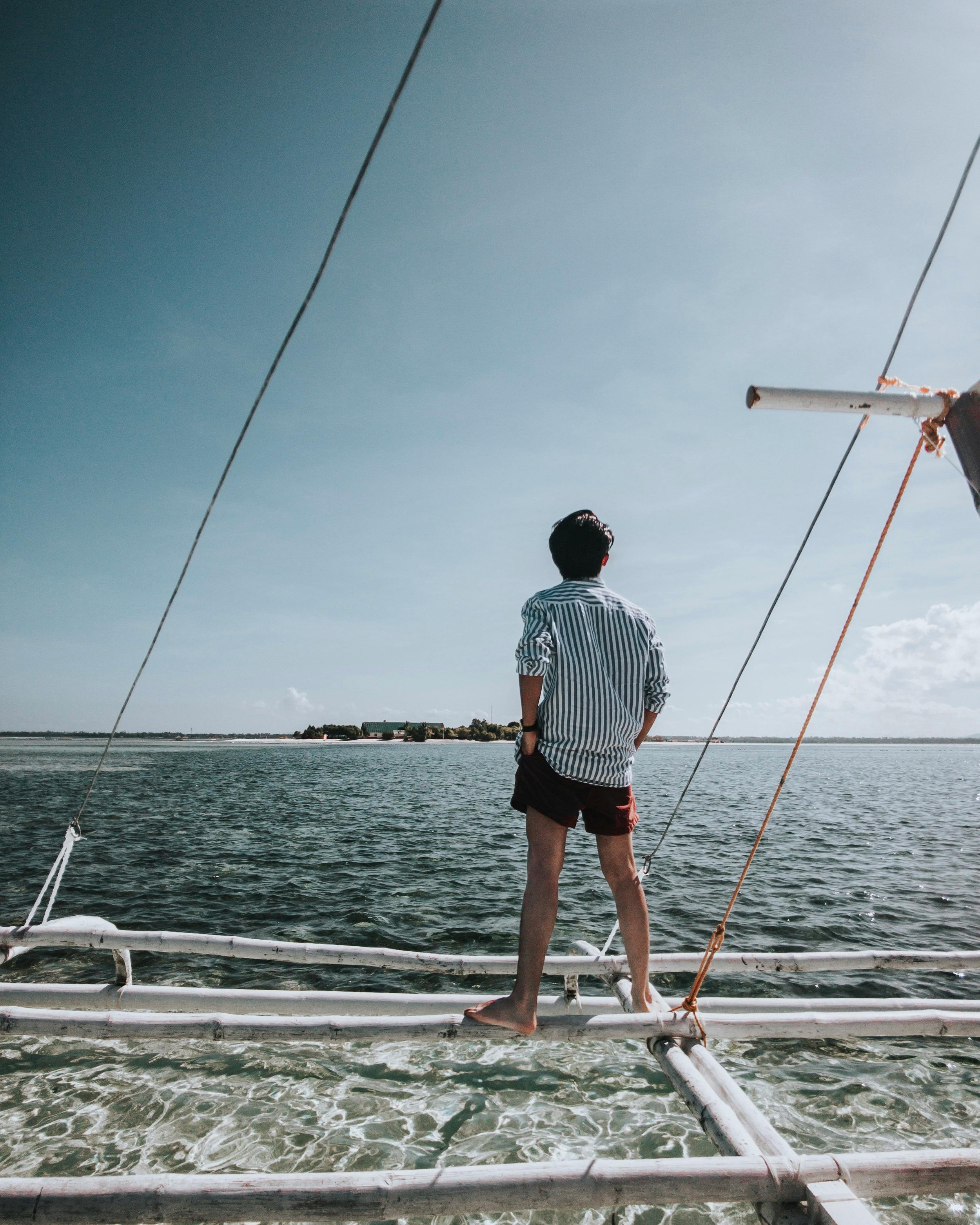 Person standing on the edge of a boat looking out over the water, with a distant shoreline and a partly cloudy sky. VOYA curates bespoke travel experiences in France and Napa Valley,