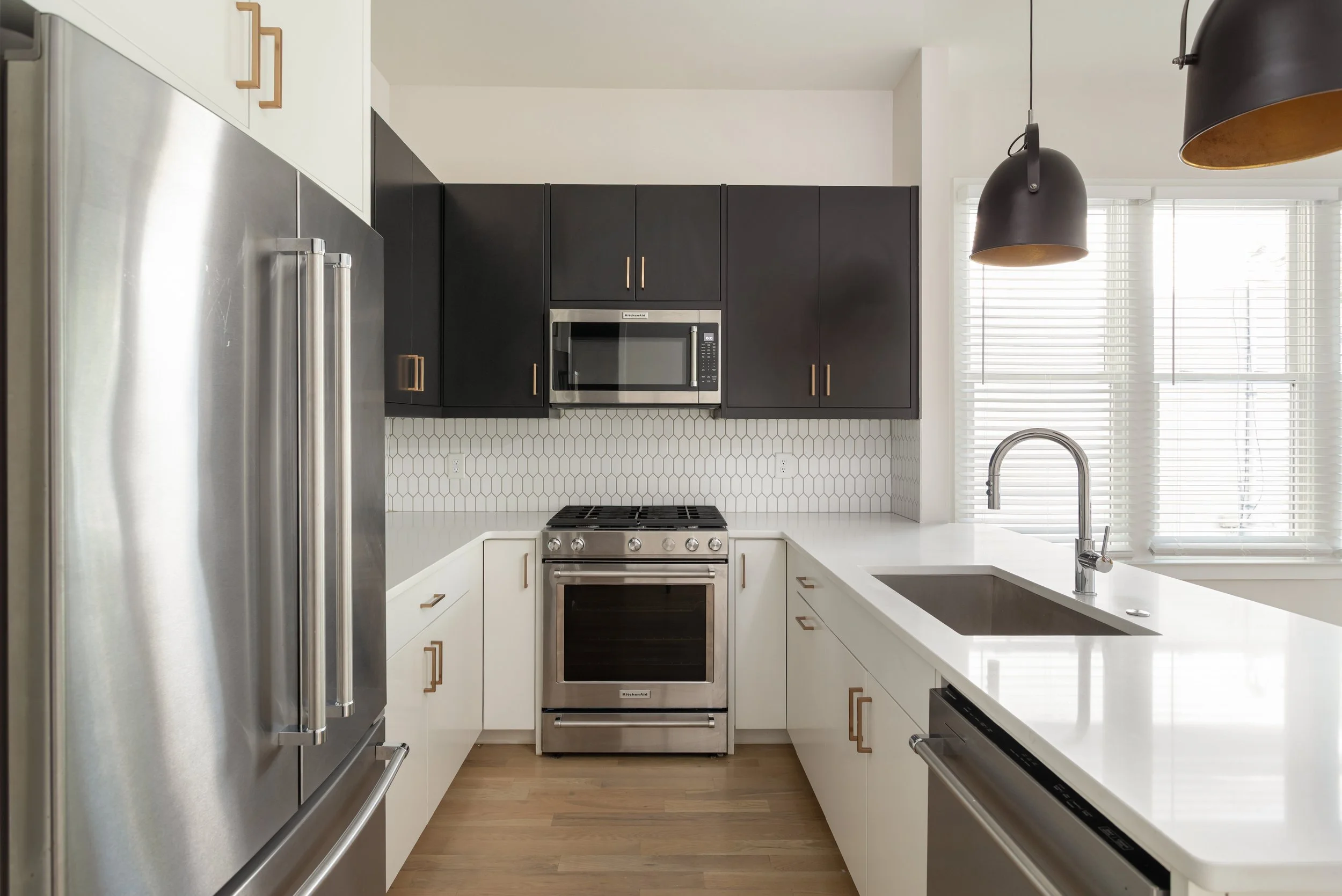 Modern kitchen with black and white cabinets, stainless steel appliances, hexagonal tile backsplash, island sink, and pendant lights