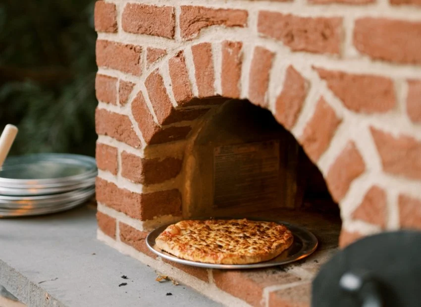A cheese pizza on a metal tray inside a brick oven.