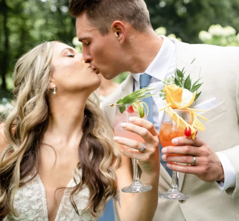 Bride and Groom kissing with signature cocktails in hand