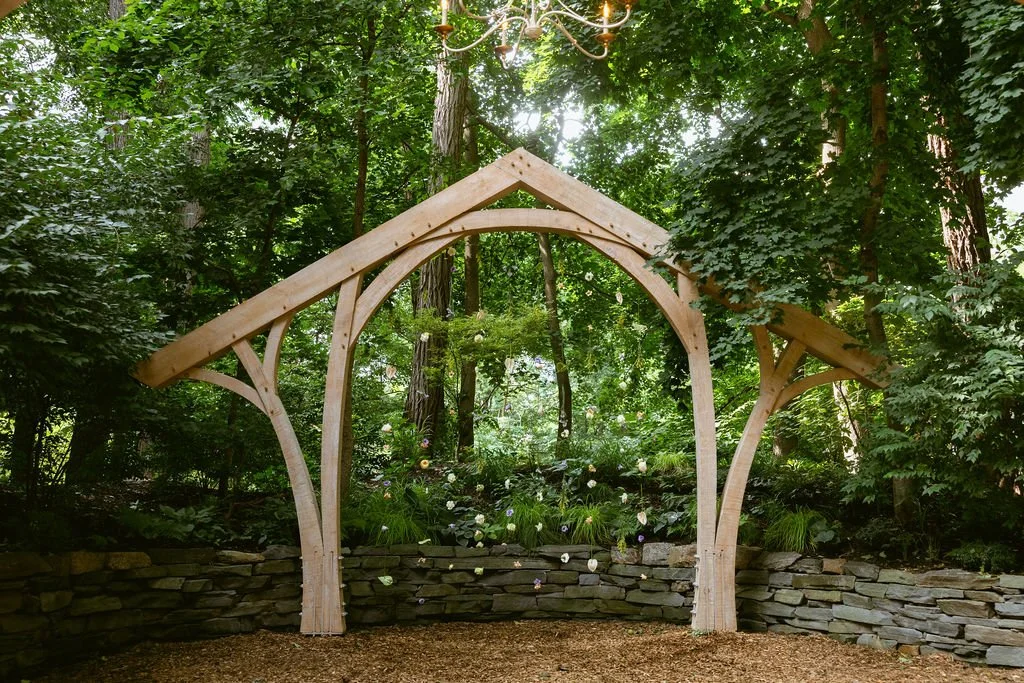 Wooden archway in a lush green outdoor garden setting surrounded by trees and plants