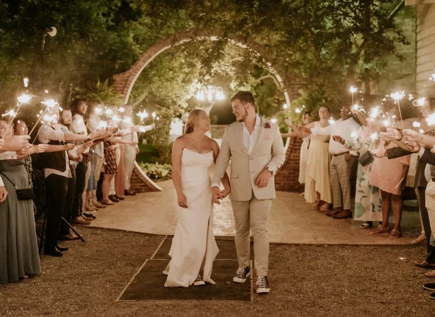 A bride and groom walk hand in hand through a path lined with guests holding sparklers at night.