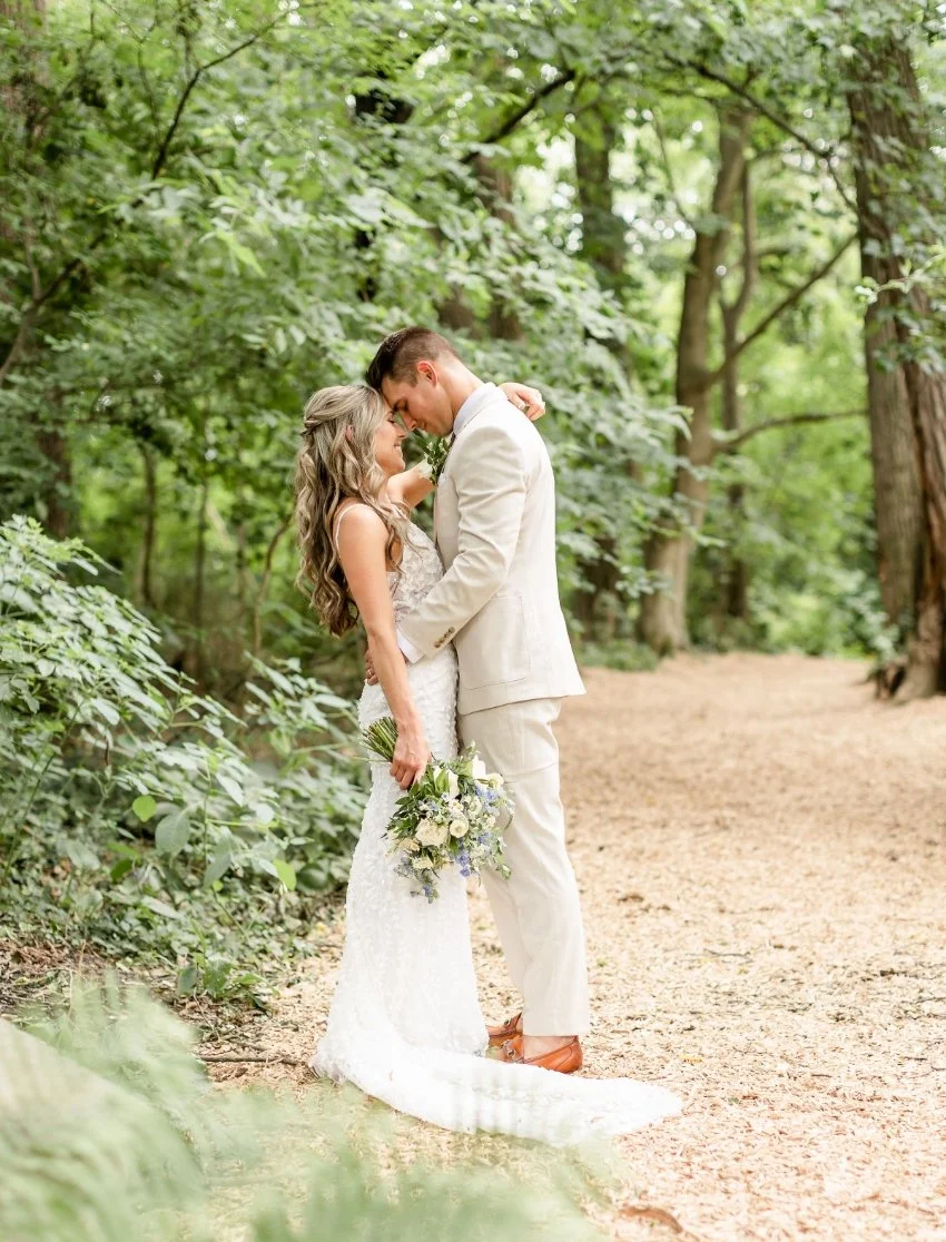 A couple dressed in wedding attire sharing a tender moment in a forest with green foliage.