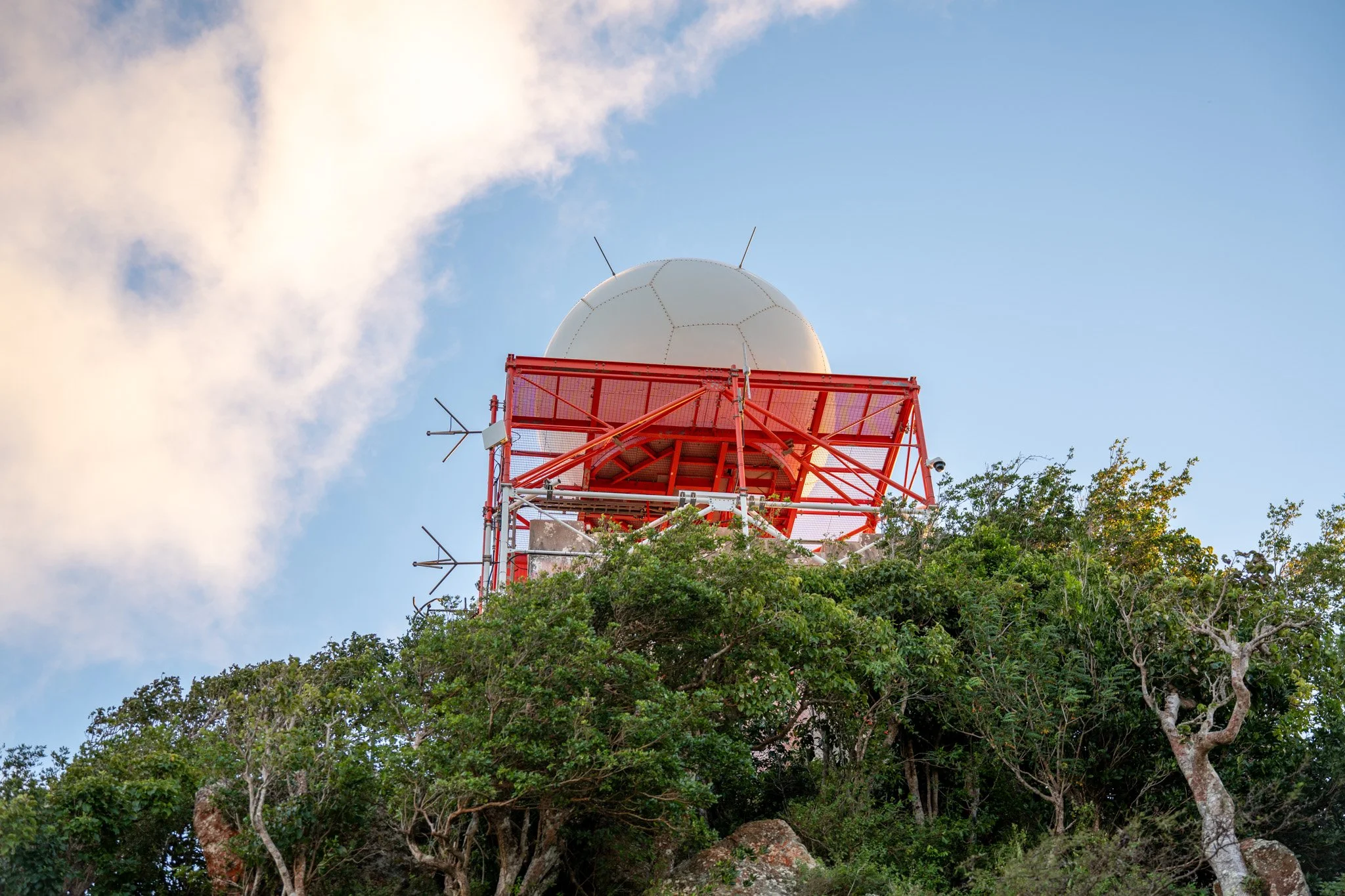 Two people celebrating on a hillside with dry grass and rocks, under a bright blue sky with white clouds.