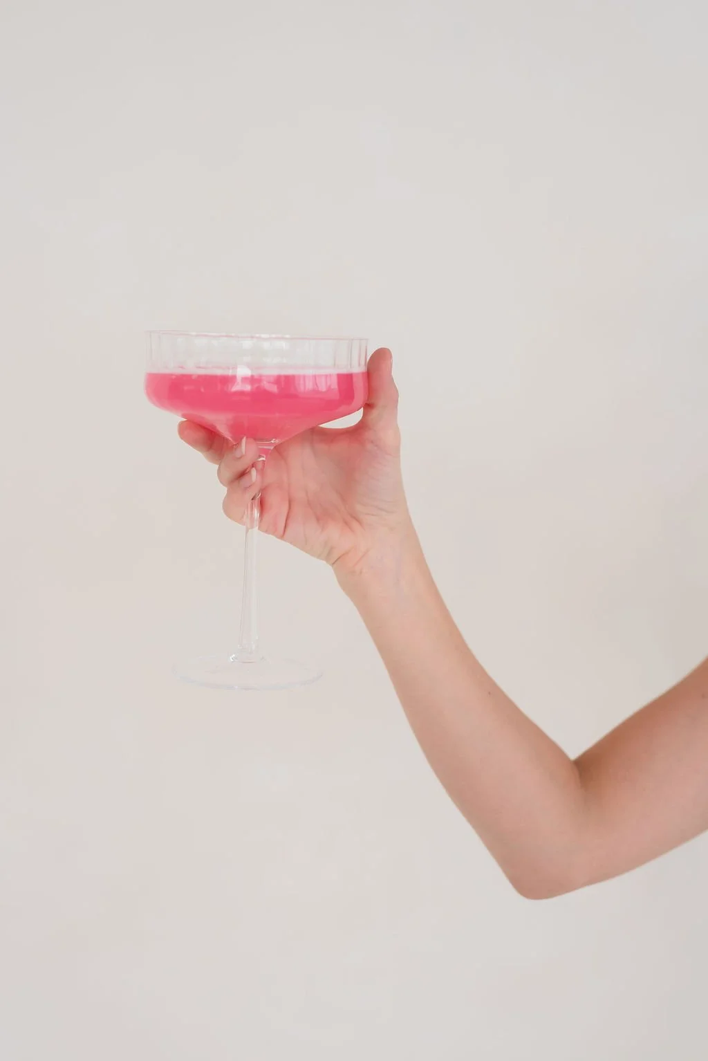 Hand raising a pink drink in a coupe glass