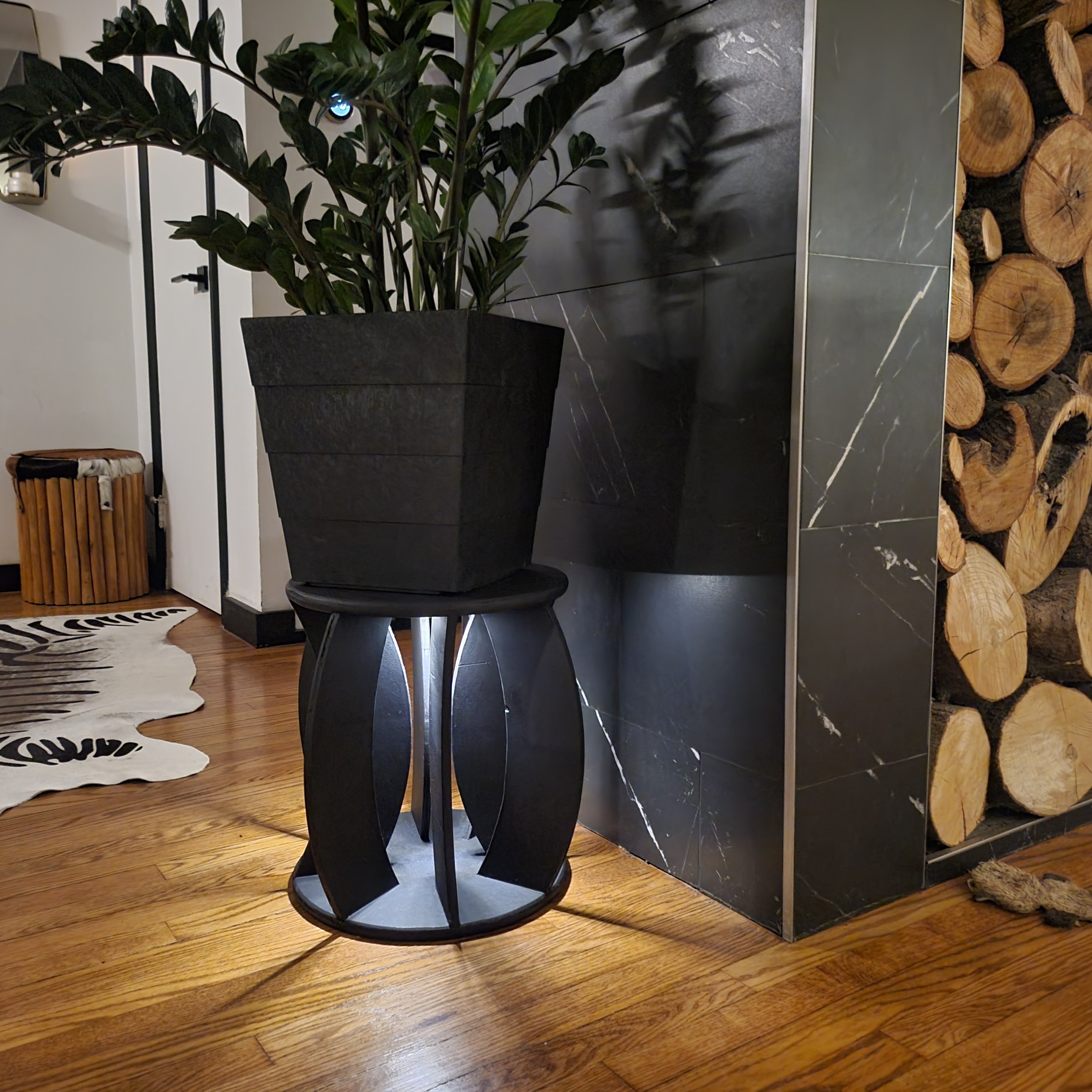 ABSTRACT PLANT STAND PLINTH PEDISTAL WITH PLANT ON TOP SITTING NEXT TO FIREWOOD