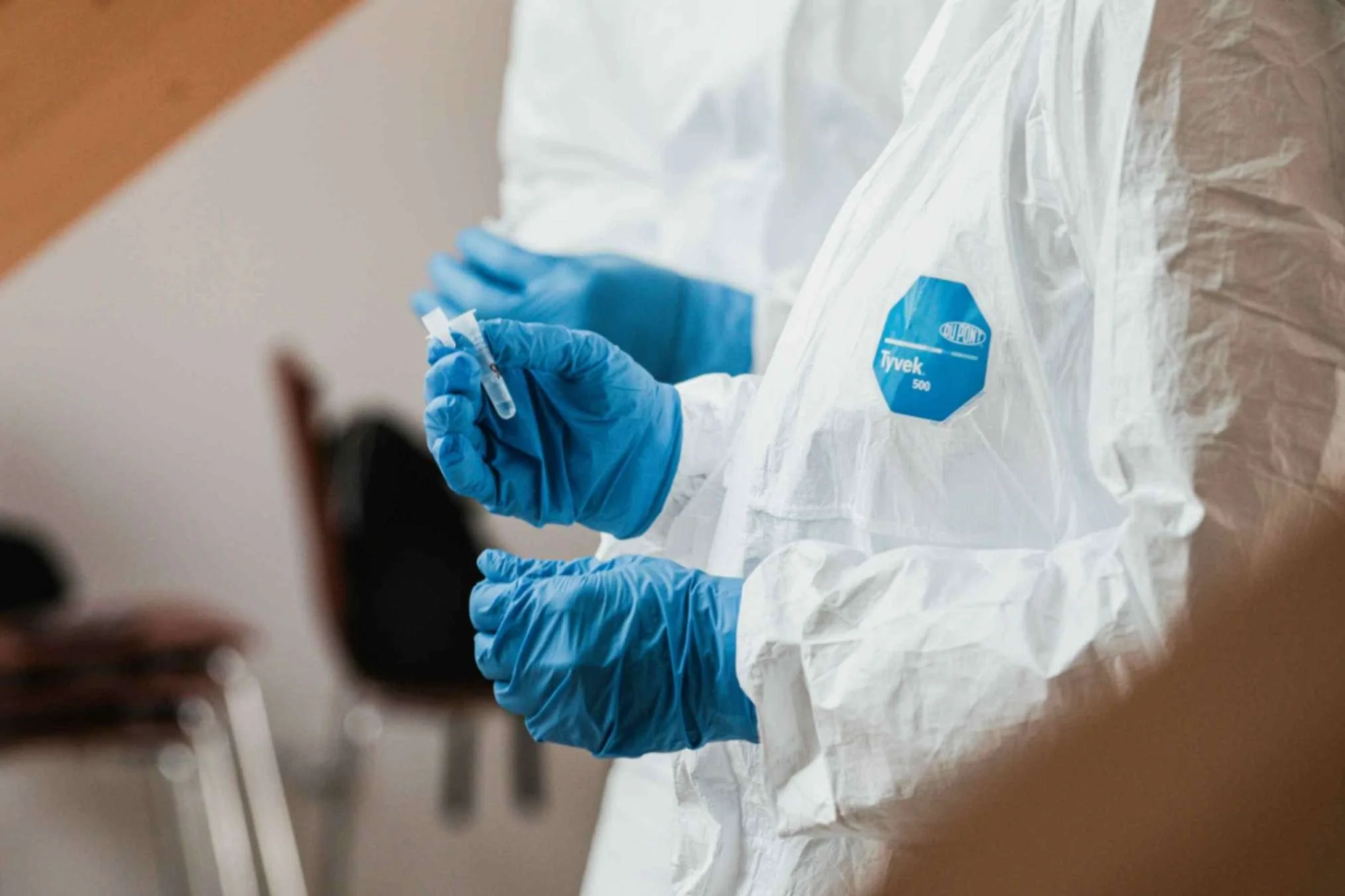 lab technicians dressed in white gowns and blue gloves testing samples in lab