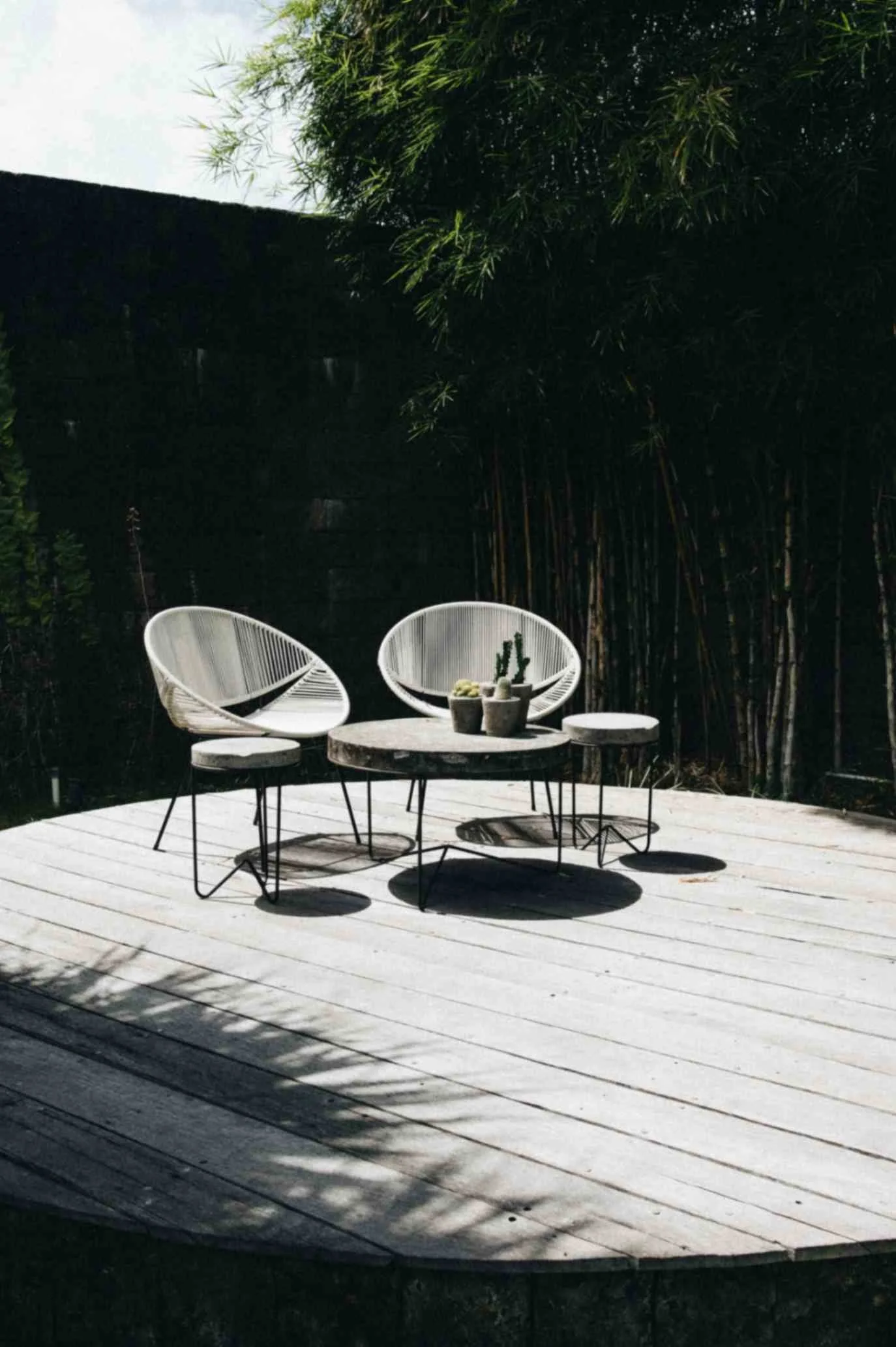 round backyard wood deck with two white chairs and patio tables surrounded by bamboo