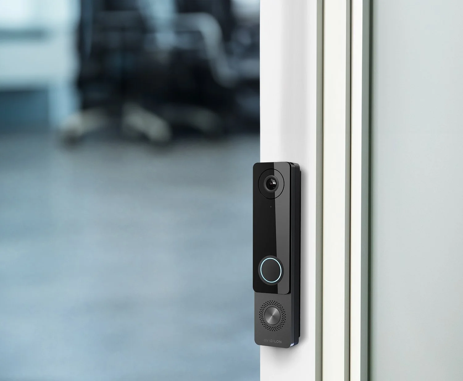 A modern video doorbell attached to a glass door frame in an indoor setting.
