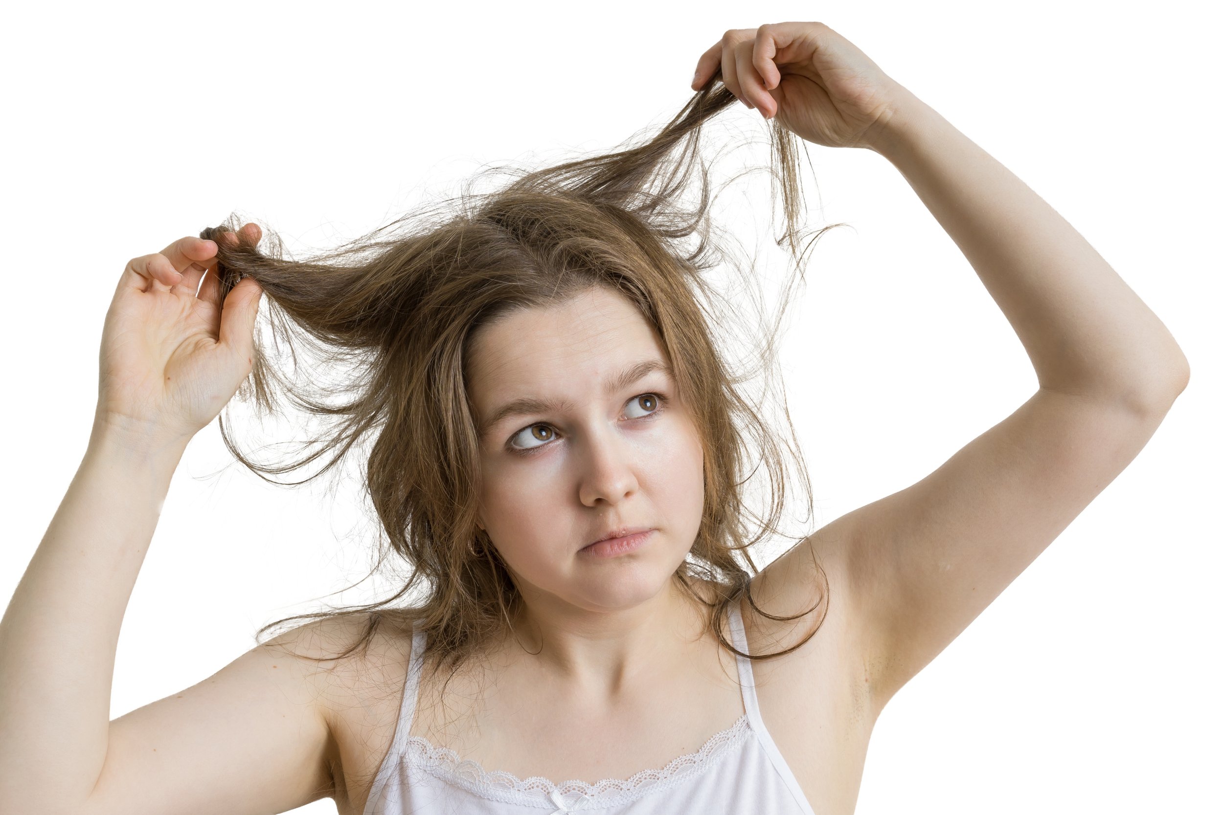 A woman with brown hair, wearing a white tank top, holding her hair and looking upward with a contemplative expression.
