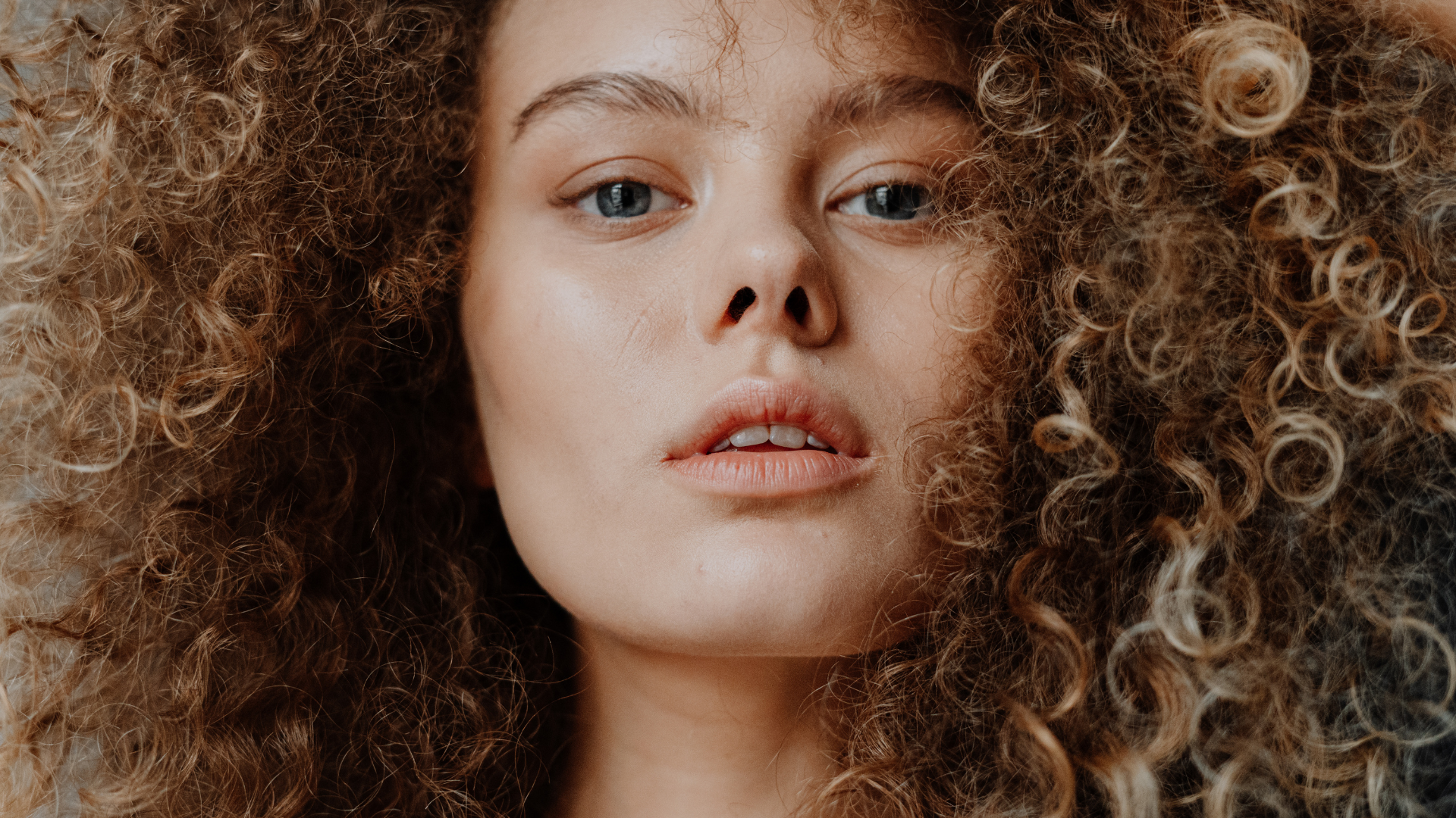 Close-up of a woman with curly light brown hair and blue eyes.