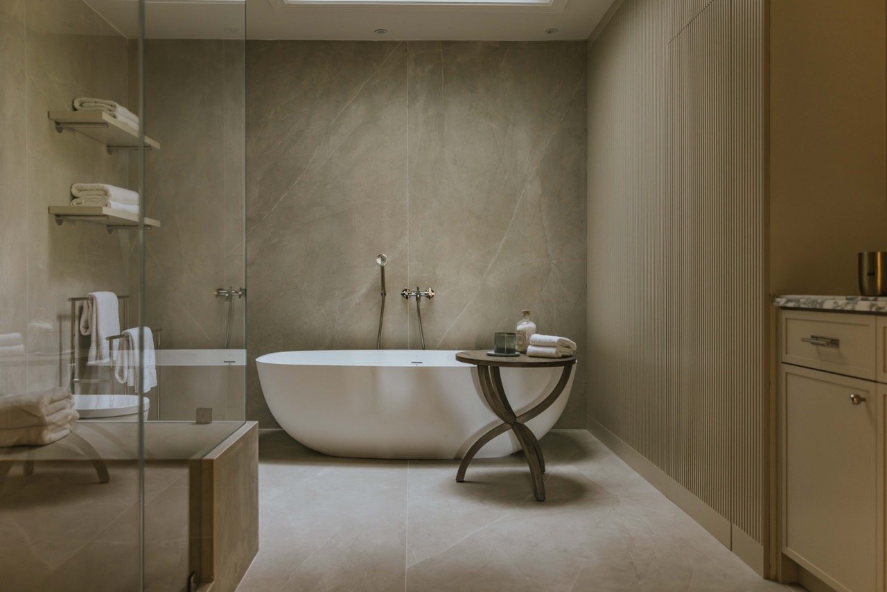 Luxury bathroom with freestanding tub, glass-enclosed shower, and shelves with towels.