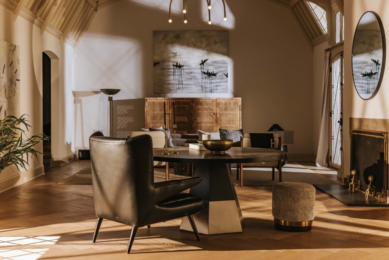 modern living room with leather chair, round table, artwork, plants, and fireplace