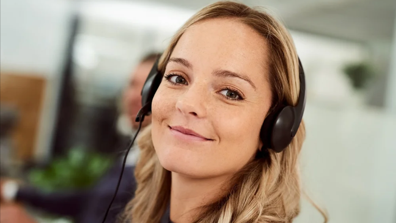 Kvindelig kundeservicemedarbejder med headset, smilende, i kontormiljø.
