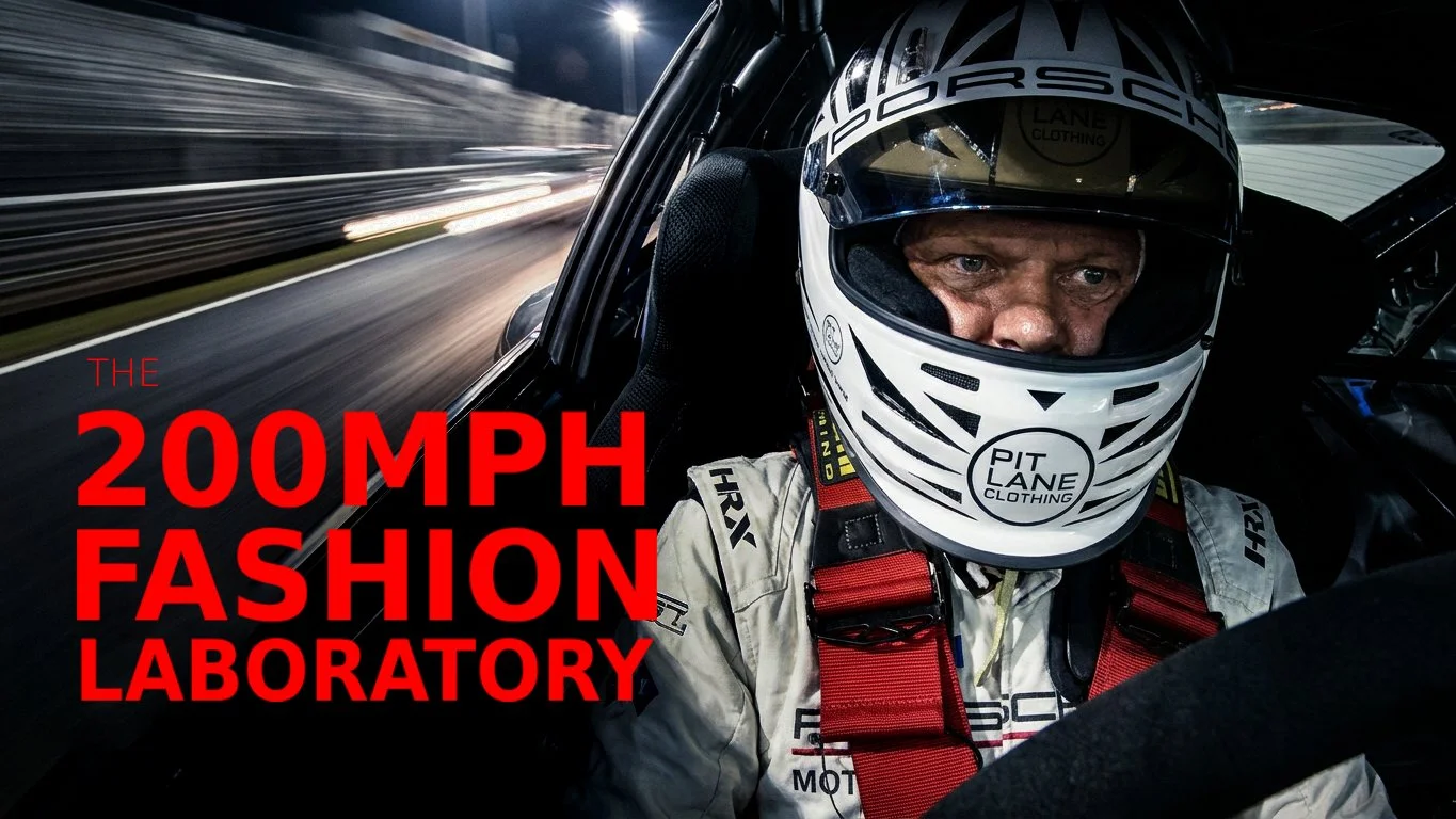 A race car driver inside a race car at night, wearing a helmet and racing suit, with a blurred race track in the background.