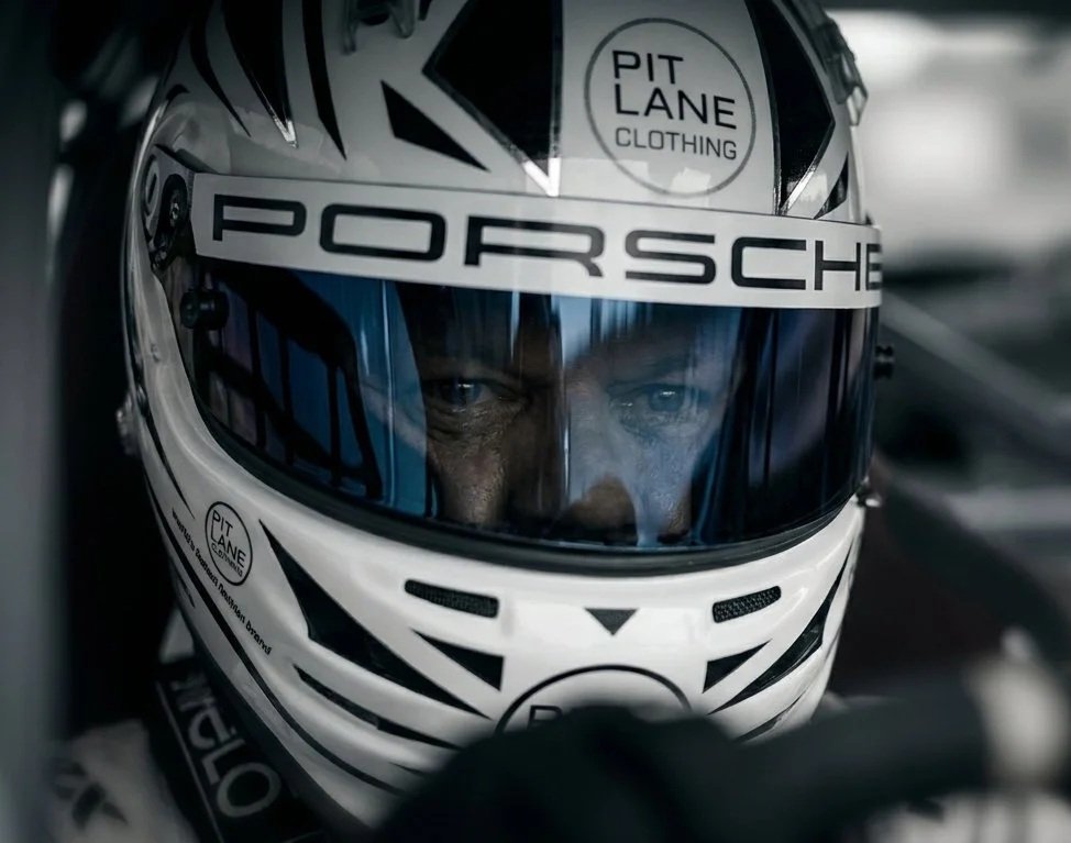 A race car driver wearing a white Porsche helmet with face shield, focused on the race.