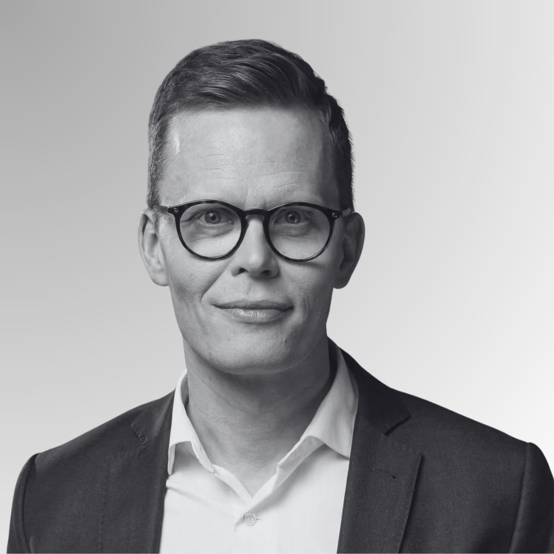 A black and white portrait of a man wearing glasses, a suit, and a tie, smiling at the camera.