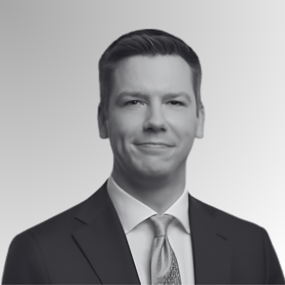 Portrait of a young man in a business suit and tie, smiling, with short hair, against a light gradient background.