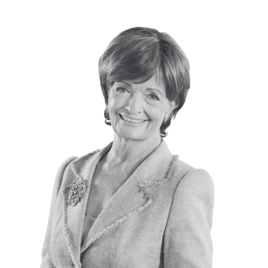 Black and white photograph of a smiling older woman with short hair, wearing a blazer with a decorative brooch.