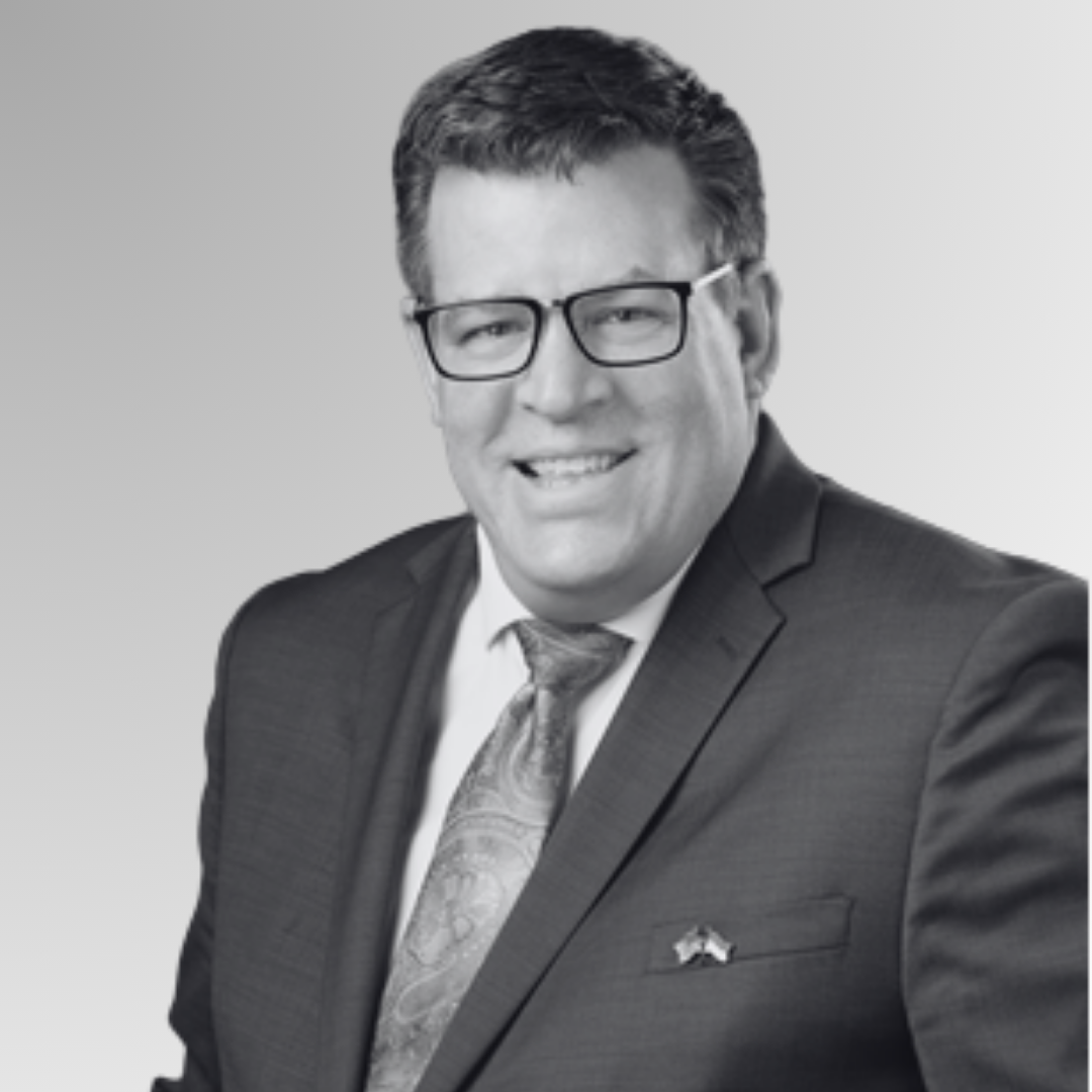 Black and white portrait of a smiling man wearing glasses, a suit, and a patterned tie.