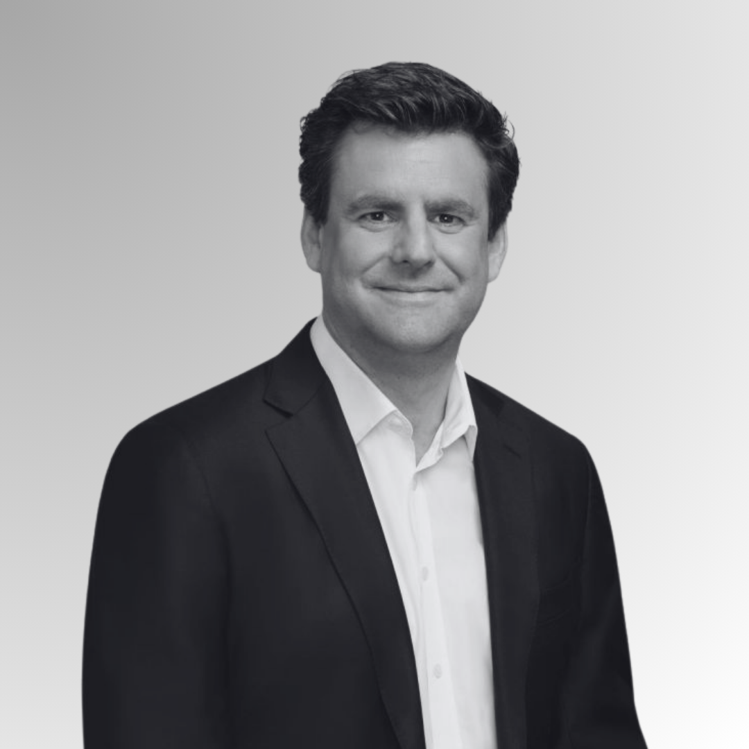 Black and white headshot of a man in a suit with short dark hair, smiling slightly, against a plain background.
