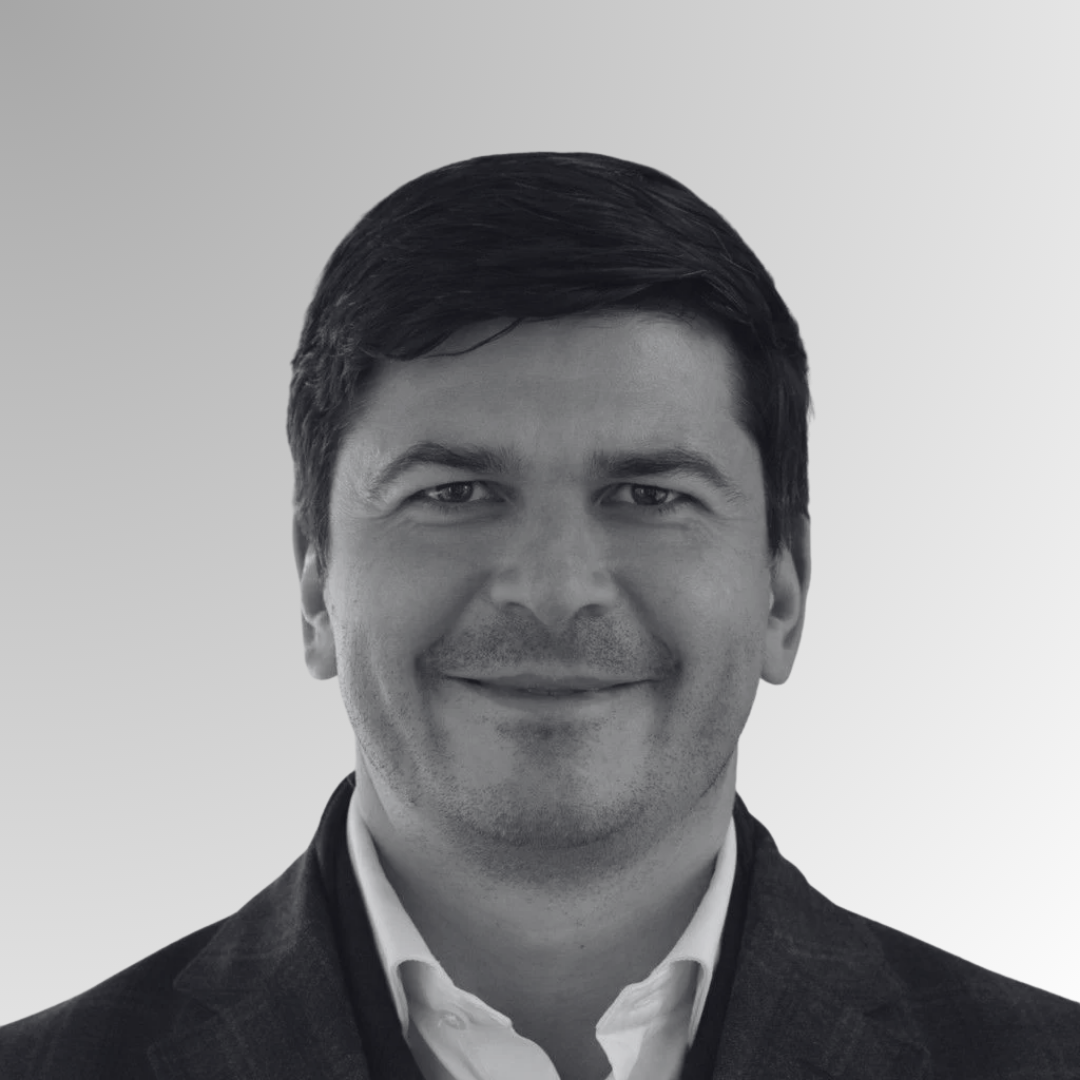 Black and white professional headshot of a smiling man in a suit and collared shirt against a plain background.