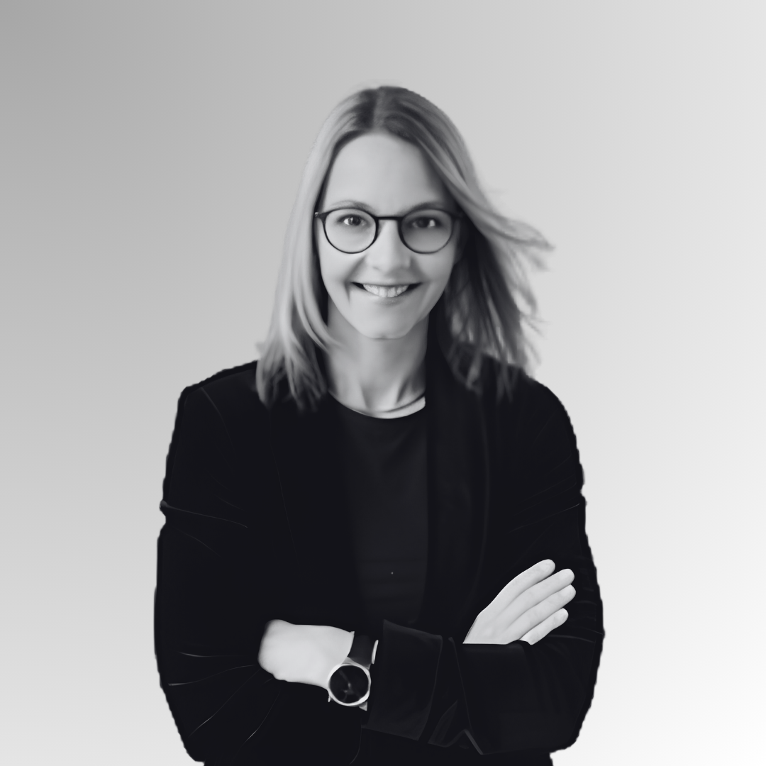 Black and white portrait of a smiling woman with glasses, crossed arms, and shoulder-length hair, wearing a blazer and casual top, against a plain gradient background.